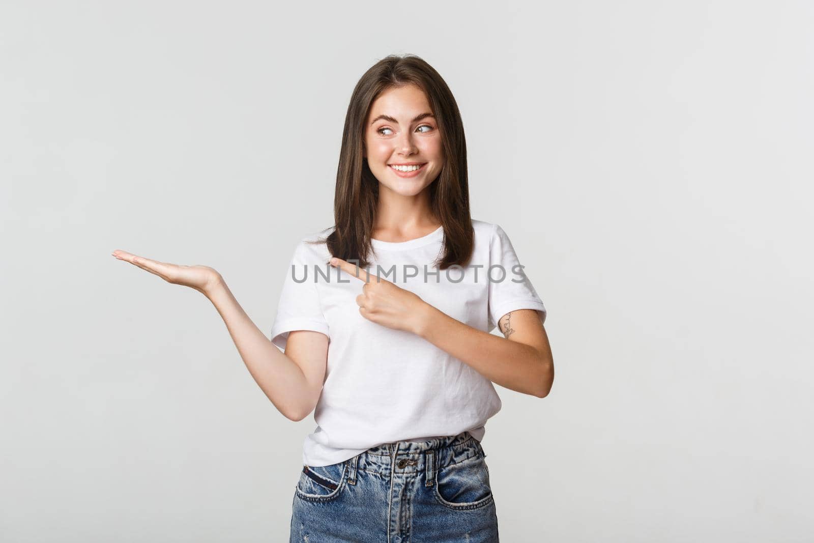 Attractive young woman pointing finger at something she holding on hand.