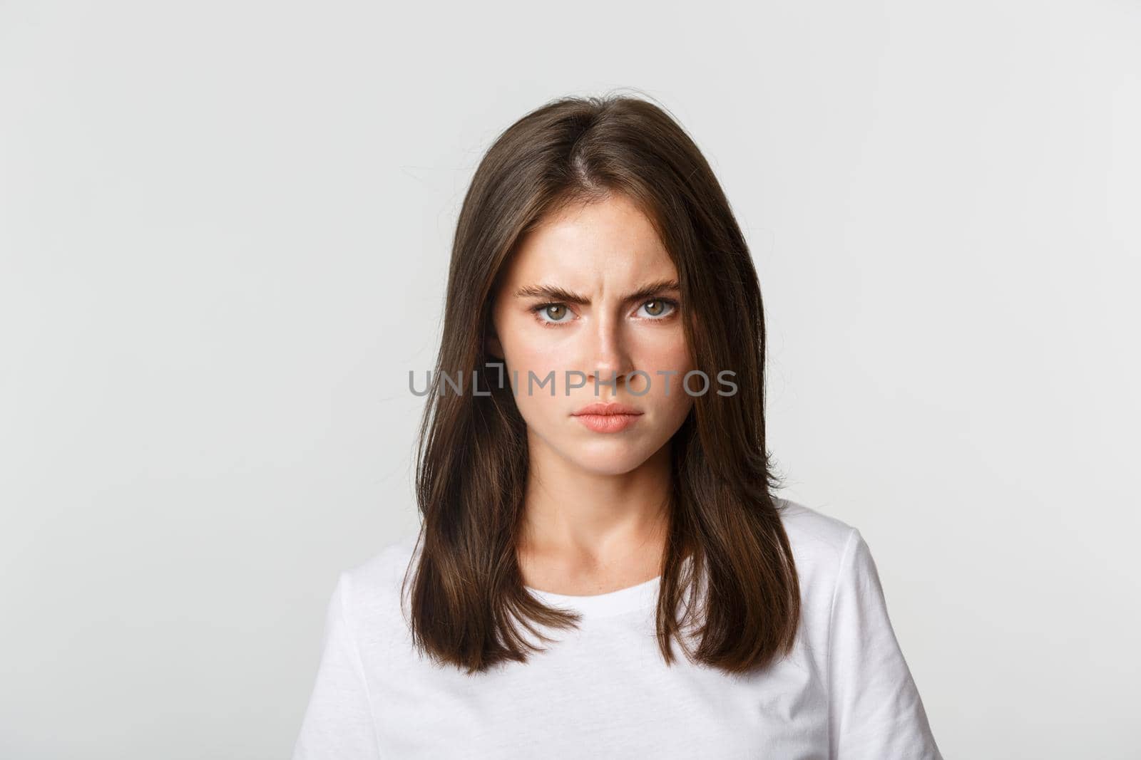 Close-up of pissed-off young girl frowning and looking angry at camera, white background.