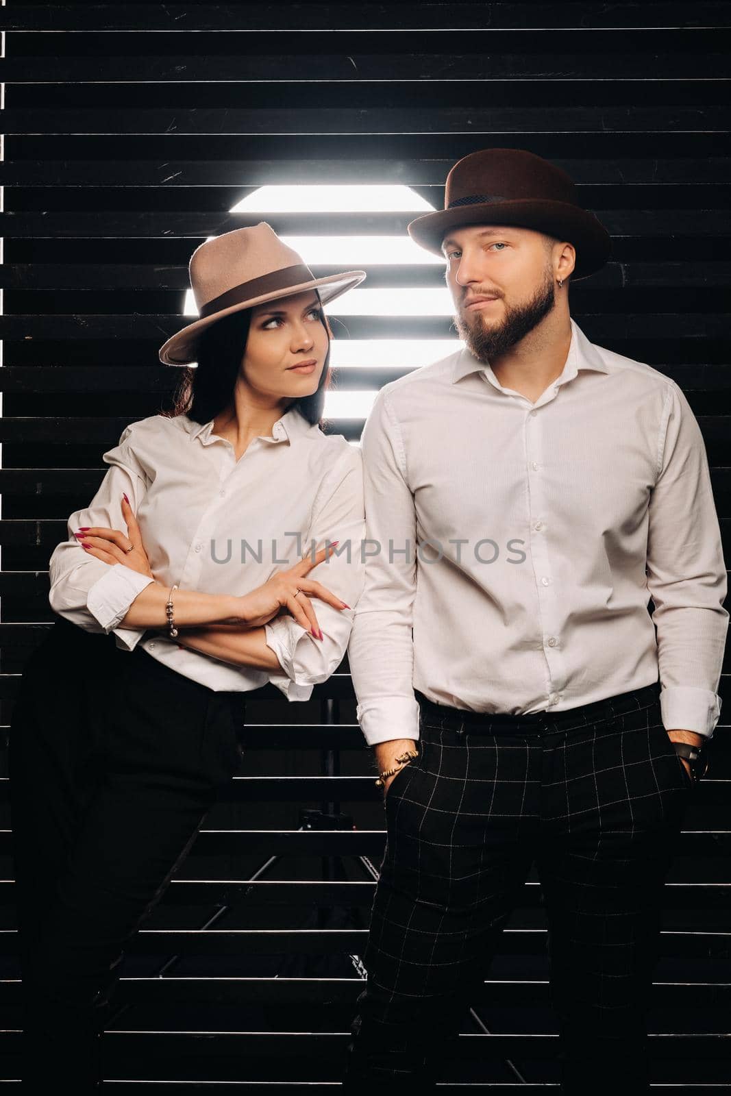 A man and a woman in white shirts and hats on a black background.A couple in love poses in the interior of the studio by Lobachad