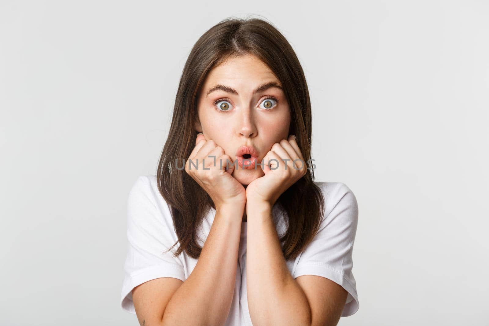 Close-up of intrigued young gossiping girl, leaning on hands and looking wondered at camera, gasping impressed, white background.