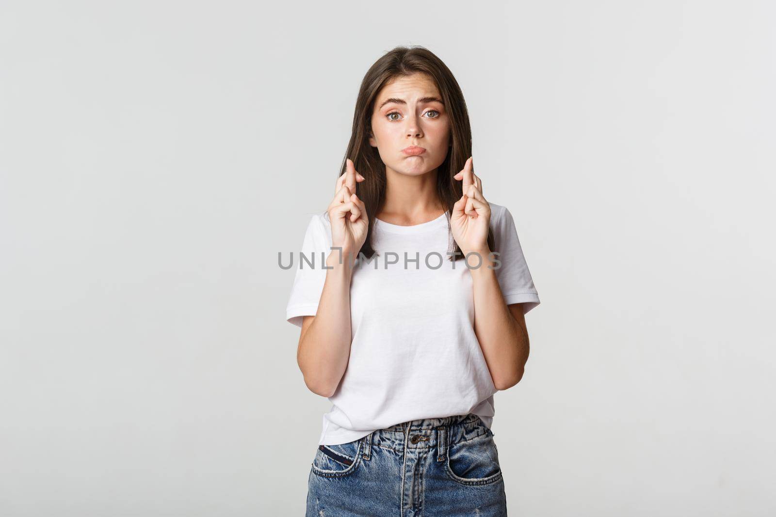 Hopeful cute brunette girl cross fingers good luck, making wish or praying.