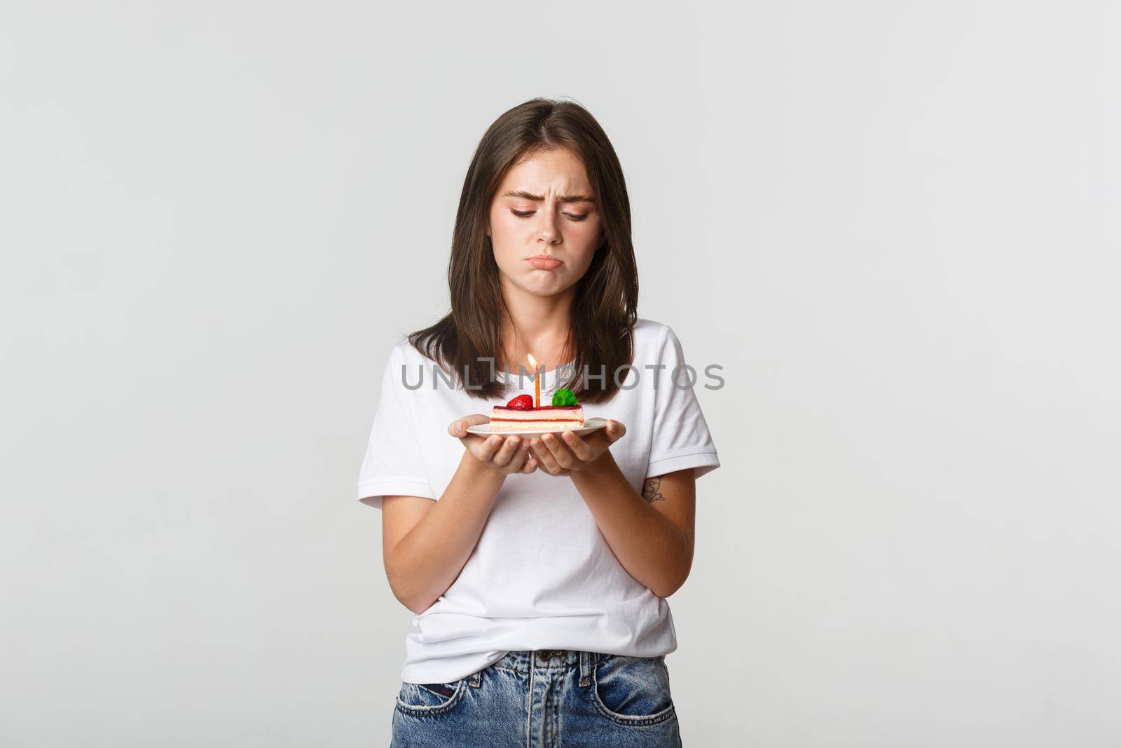Miserable birthday girl looking sad at b-day cake with candle.