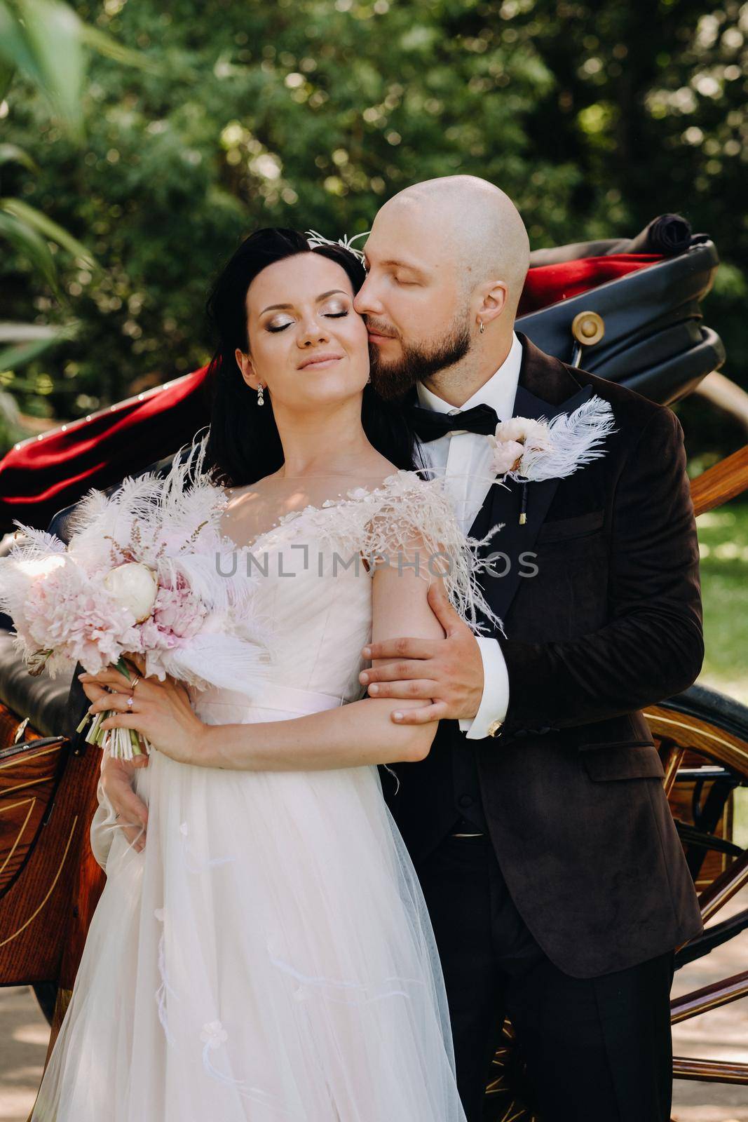 A couple of the bride and groom are standing near the carriage in nature in retro style.