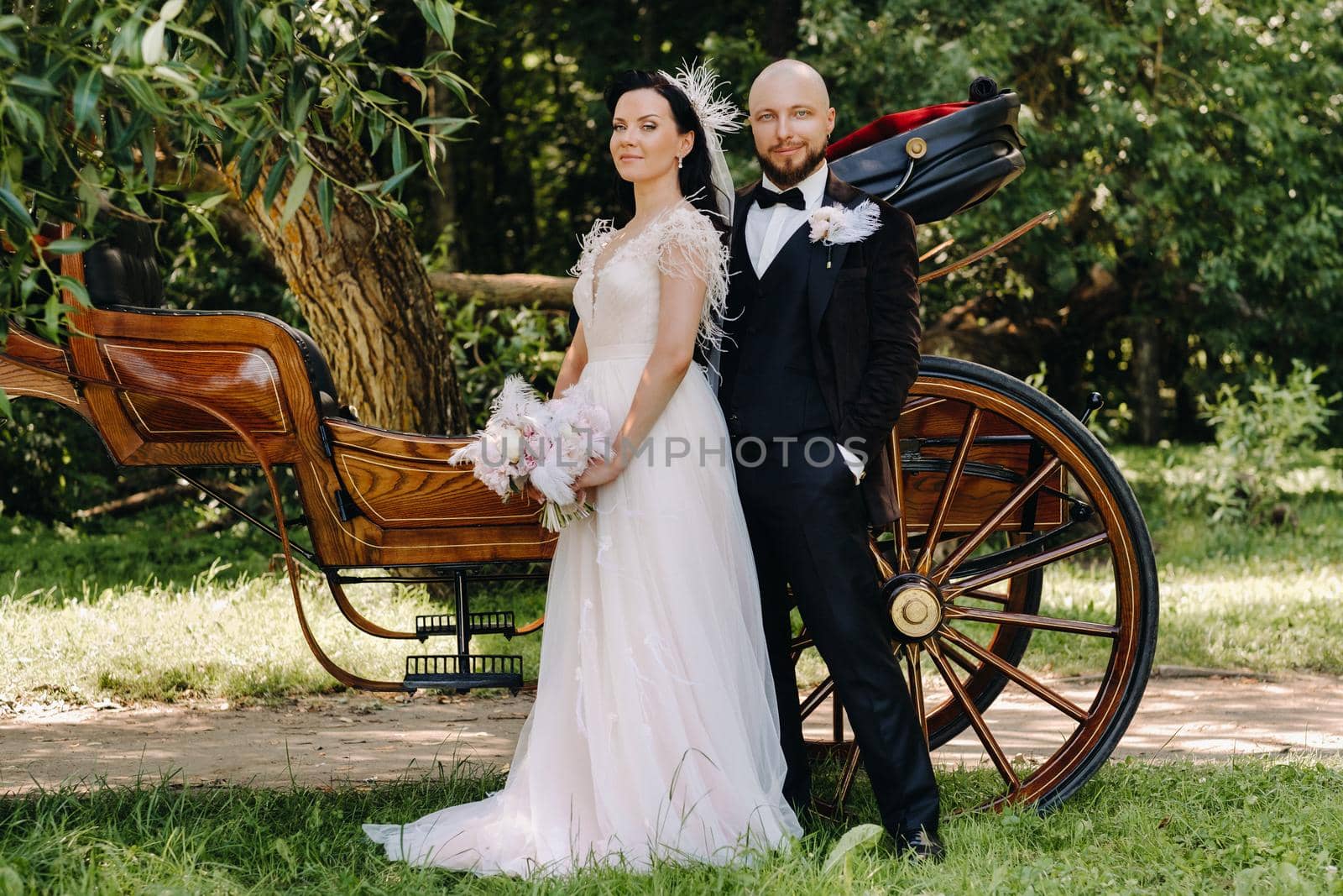 A couple of the bride and groom are standing near the carriage in nature in retro style.