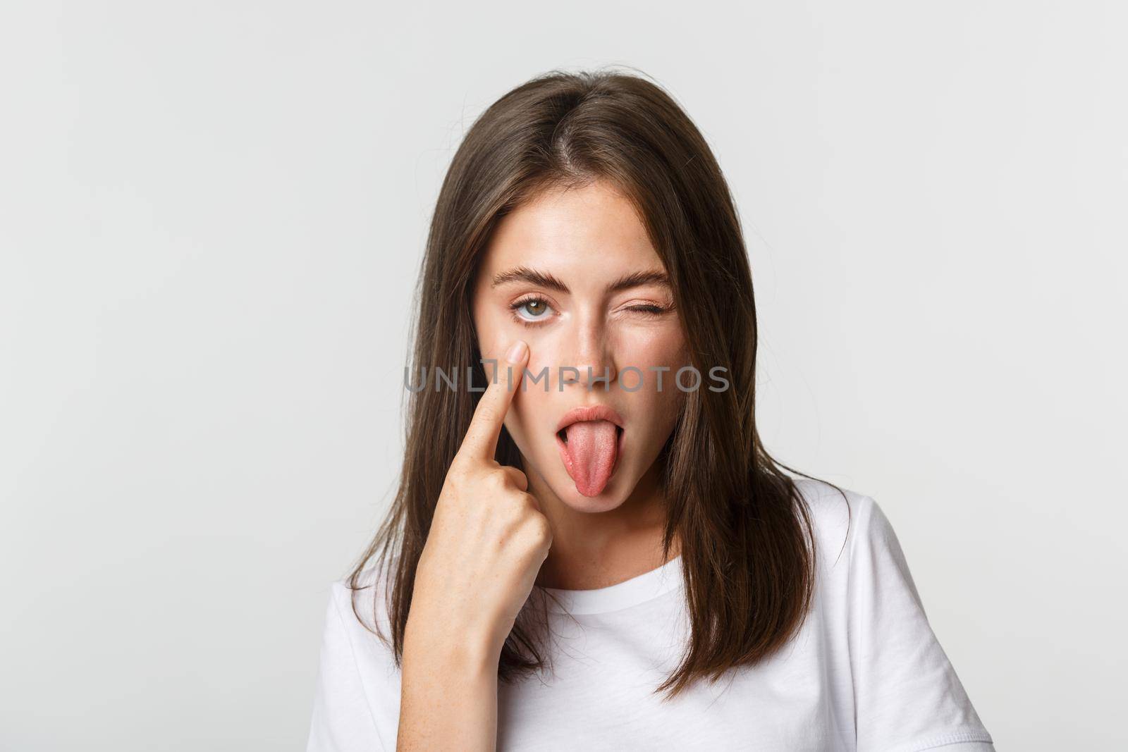 Close-up of silly attractive young girl showing tongue and pulling eyelid, watching you.