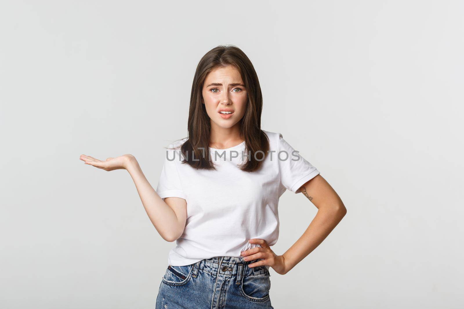 Skeptical and unamused young bothered girl shrugging, raise one hand displeased.