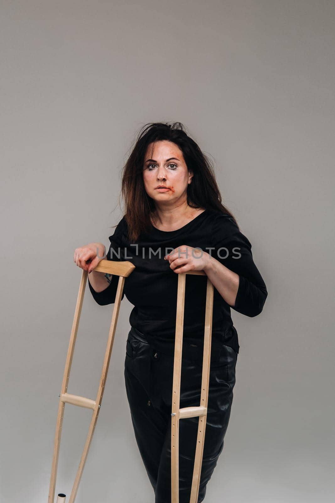 A battered woman in black clothes with casters in her hands on a gray background.