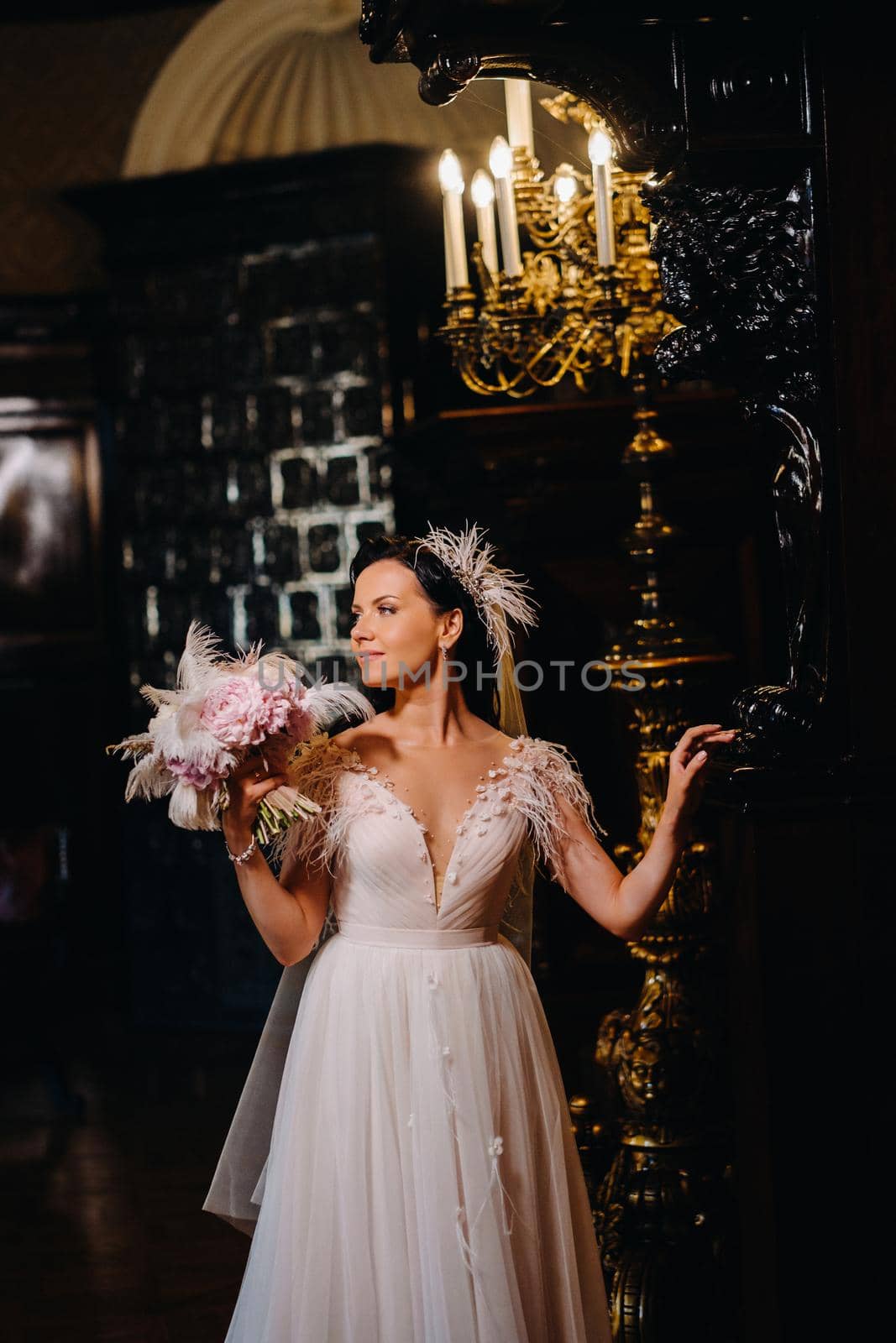 The bride in a wedding dress and with a bouquet stands at the old interior of the castle.