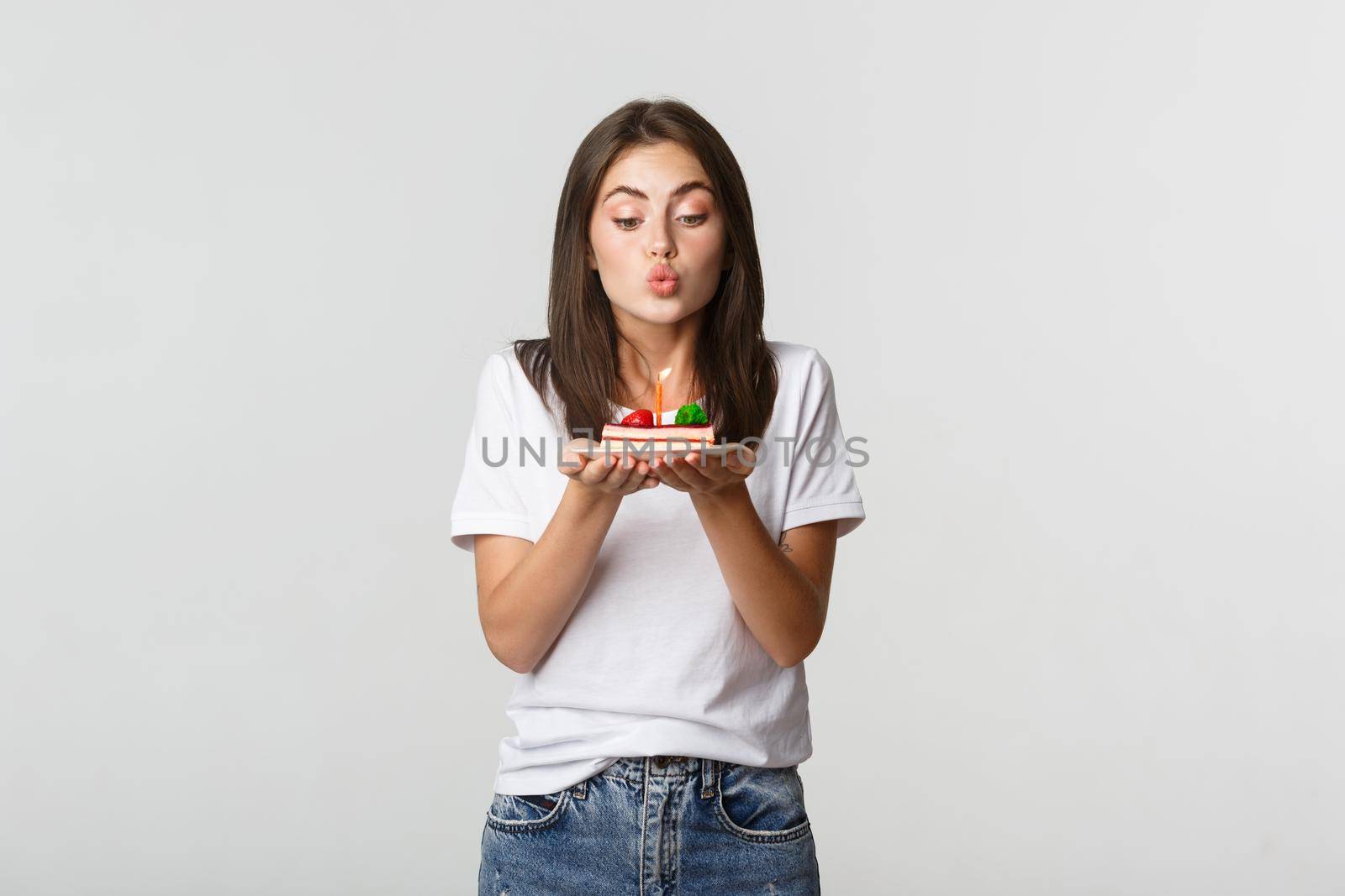 Excited and dreamy cute birthday girl making wish on b-day cake, blowing candle.