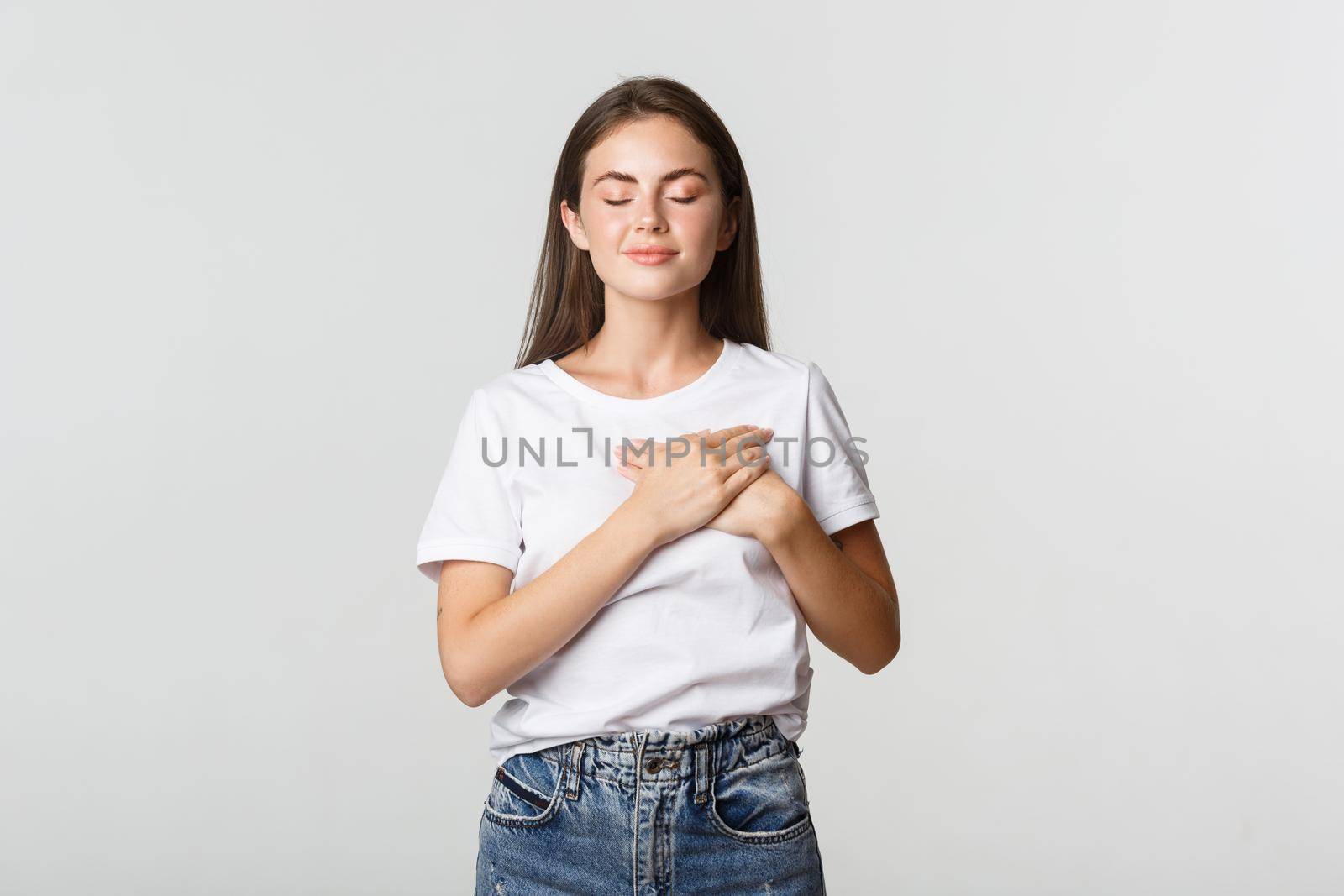 Portrait of tender and dreamy smiling woman, close eyes and holding hands on heart, daydreaming.