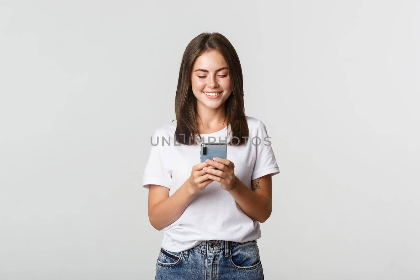 Smiling attractive girl using mobile phone and looking at screen pleased by Benzoix