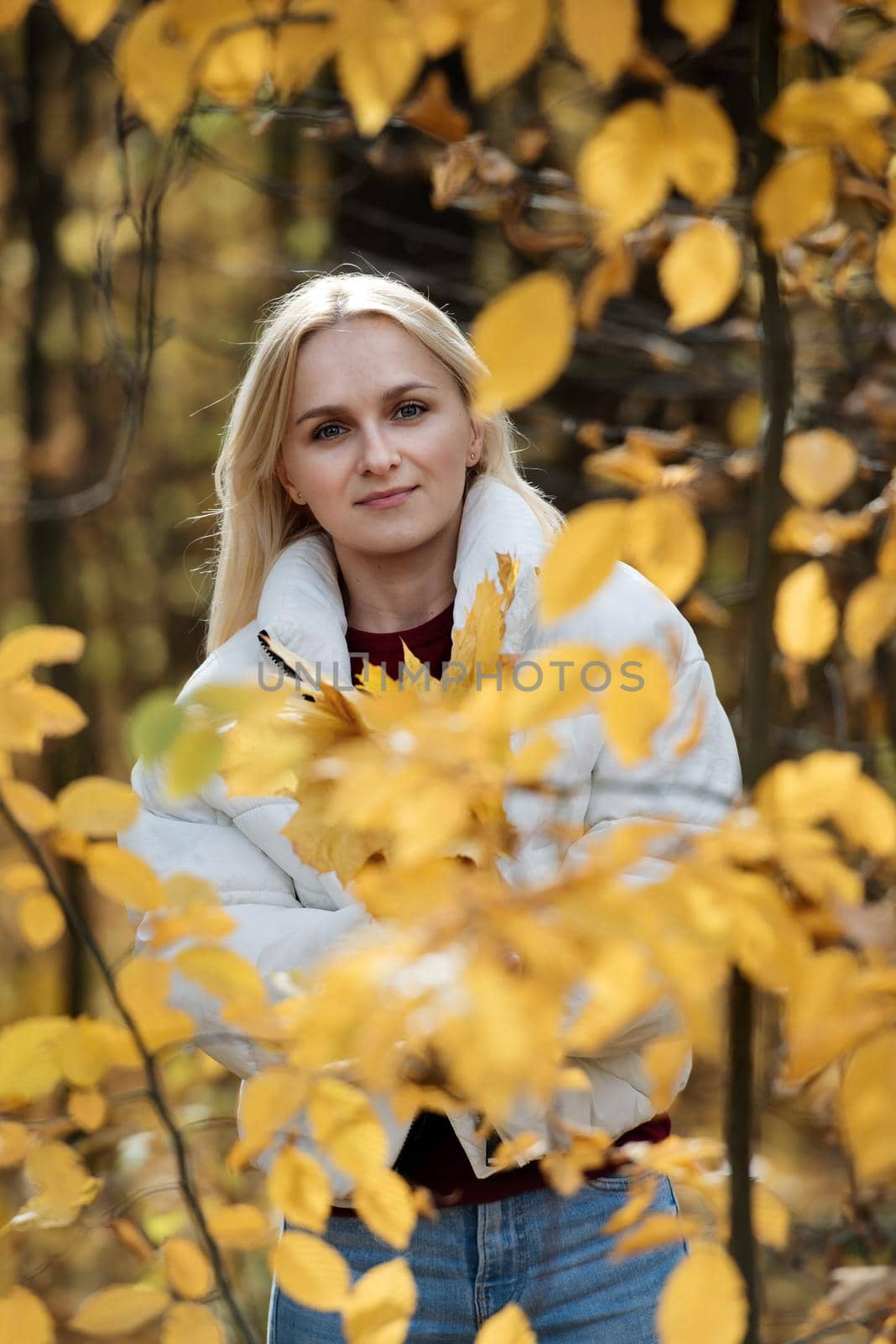 Portrait of a young blonde woman in the autumn forest, with a bouquet of yellow leaves in her hands.