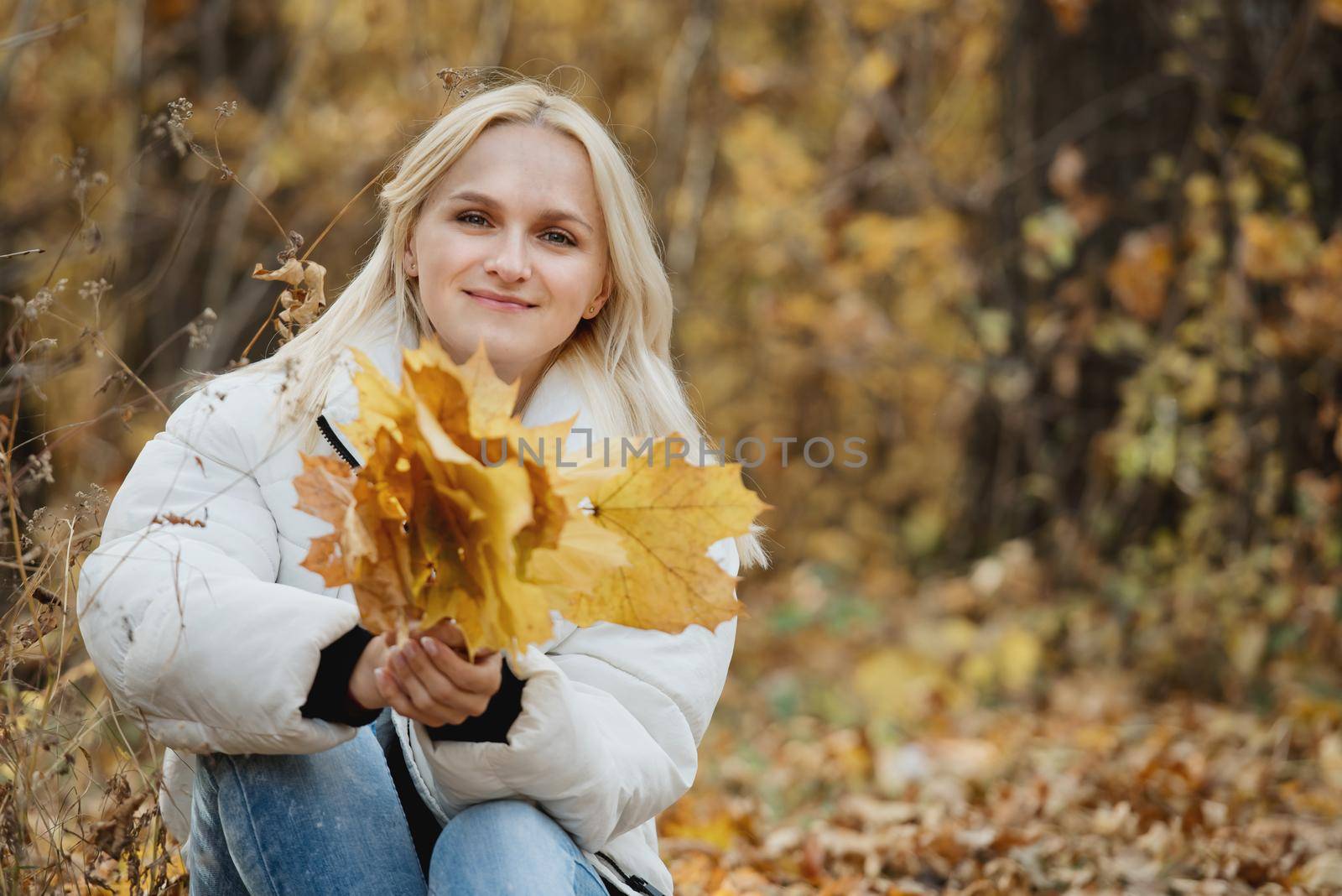 Portrait of a young blonde woman in the autumn forest, with a bouquet of yellow leaves in her hands. by leonik