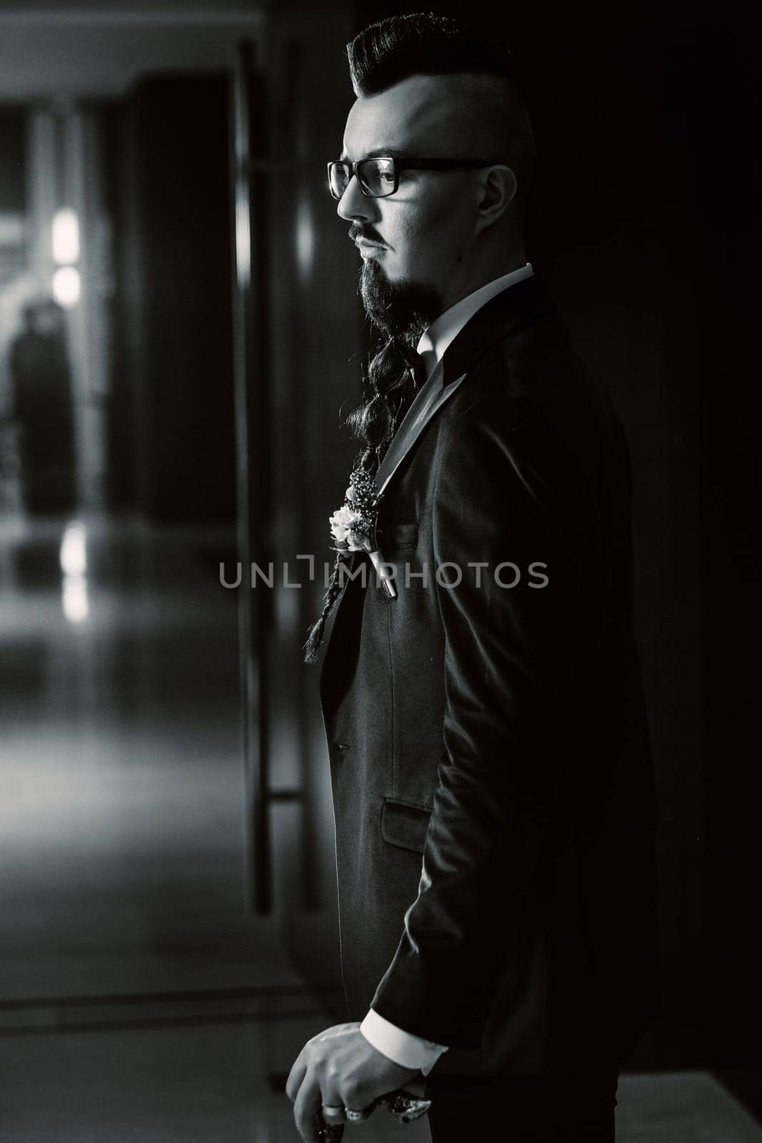 The groom in a tuxedo and bow tie with a mohawk hairstyle and a cane in the interior. black and white photo.