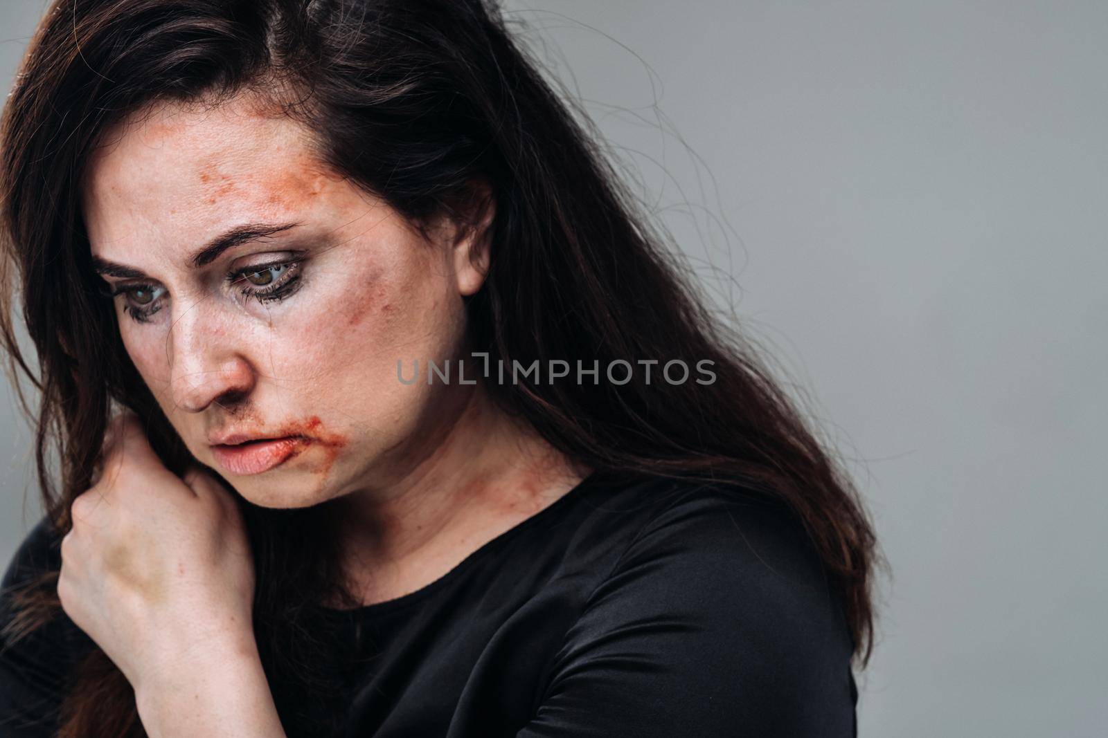 a battered woman in black clothes on an isolated gray background. Violence against women.
