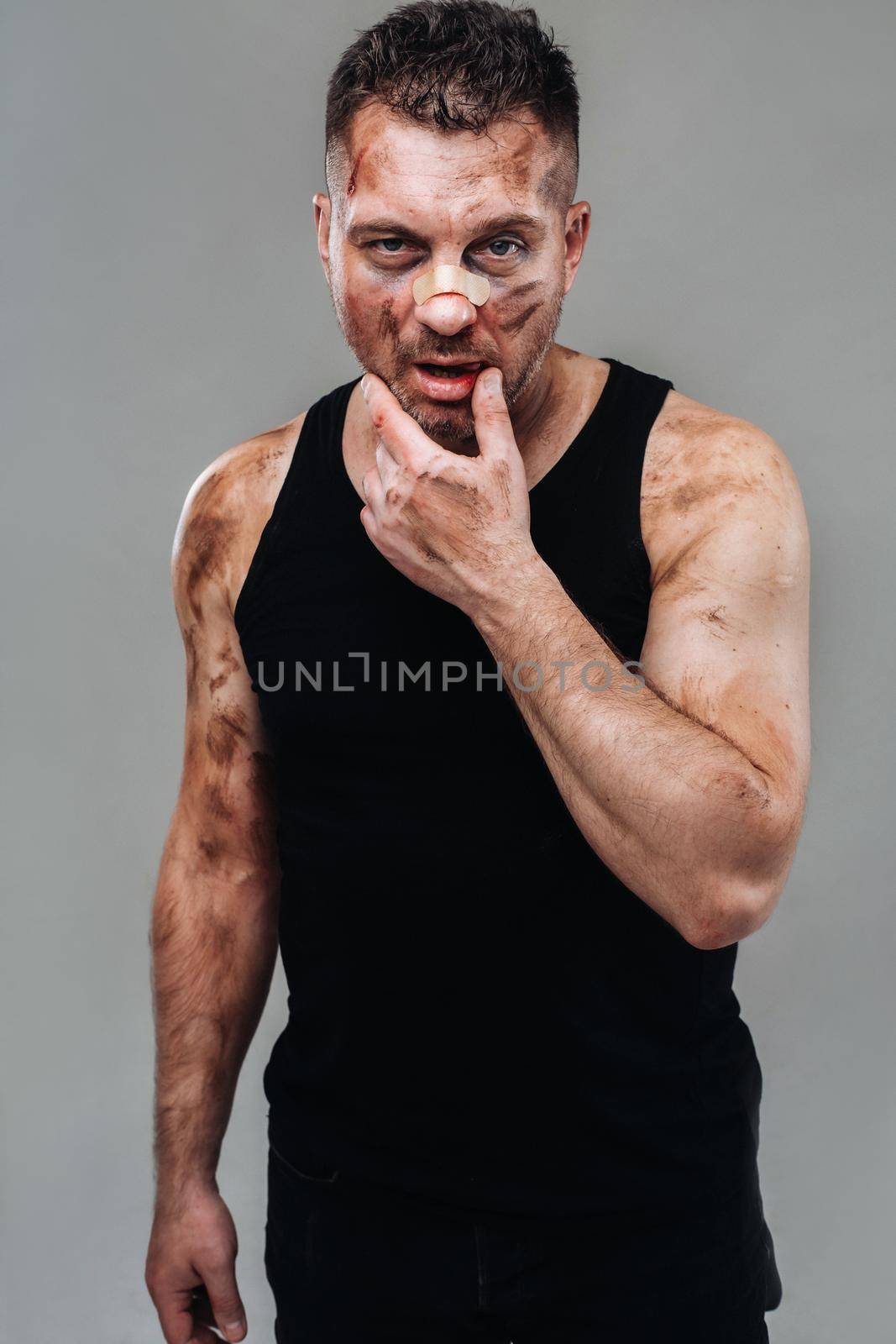 a battered man in a black T shirt who looks like a drug addict and a drunk stands against a gray background.