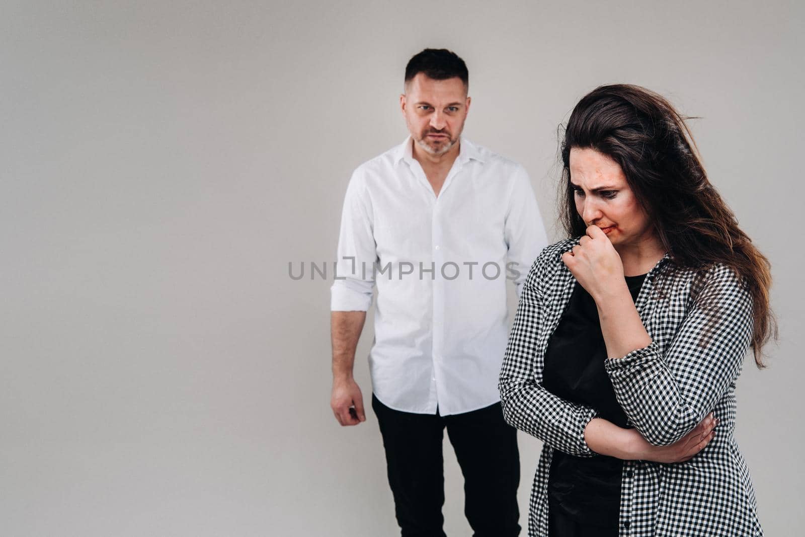 A woman beaten by a man stands on a gray background. Domestic violence.