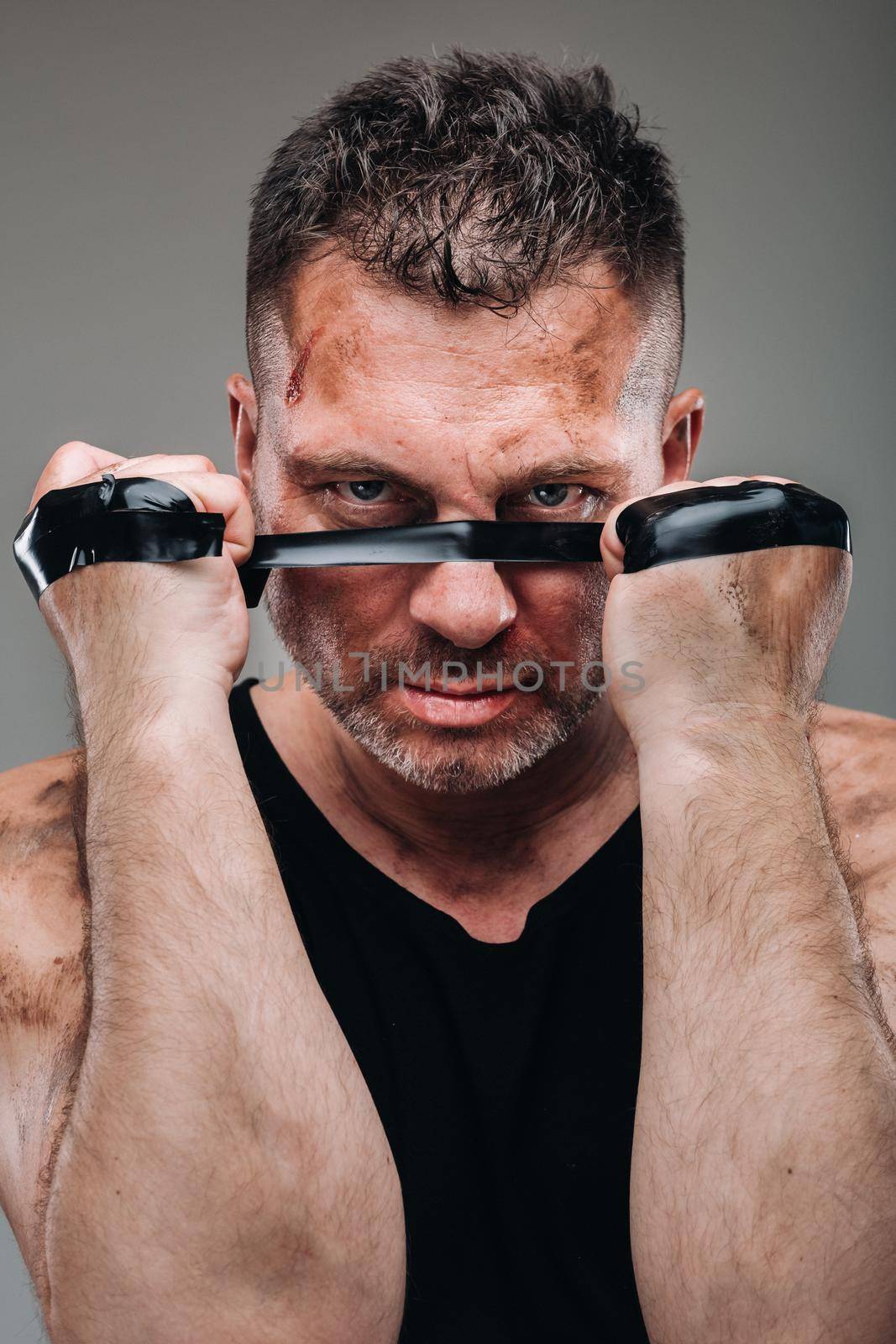 on a gray background stands a battered man in a black T shirt looking like a fighter and preparing for a fight.