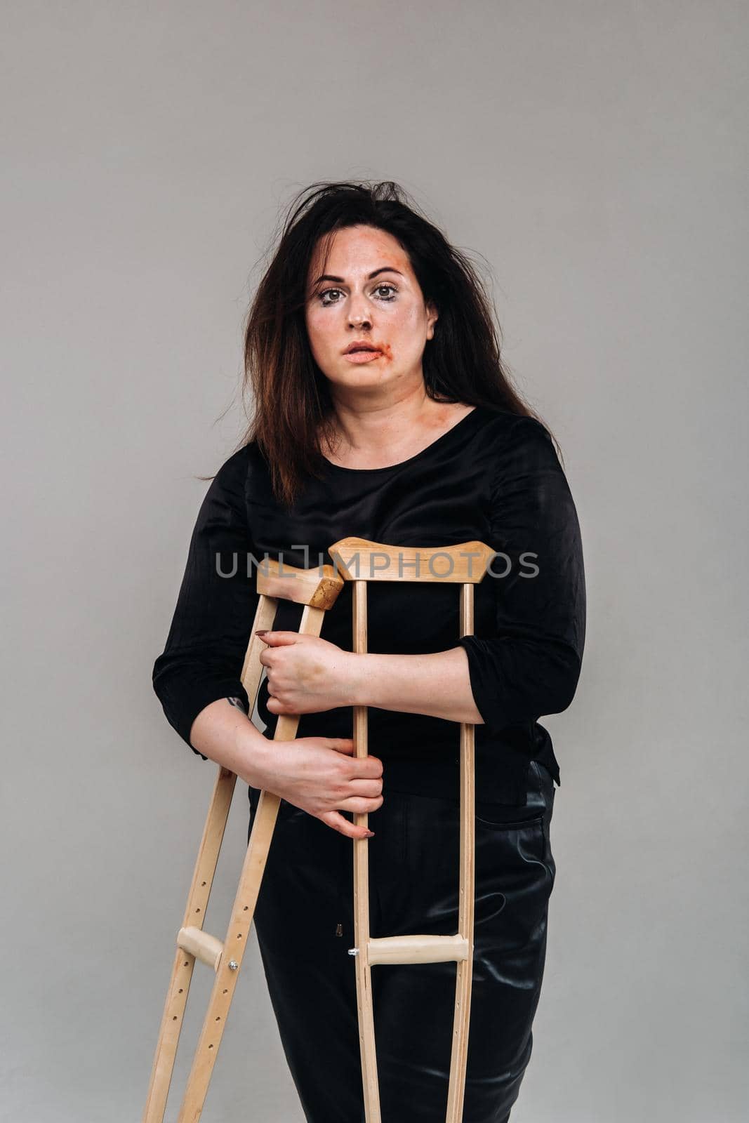 A battered woman in black clothes with casters in her hands on a gray background.