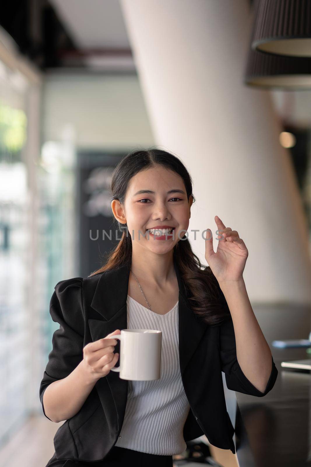 portrait smiling asian business woman pointing up and looking at the camera in modern office by nateemee
