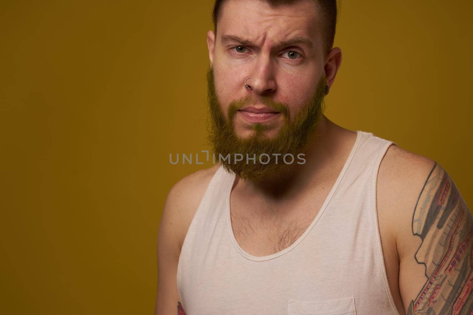 a bearded man with a serious expression in a white t-shirt with tattoos on his arms. High quality photo