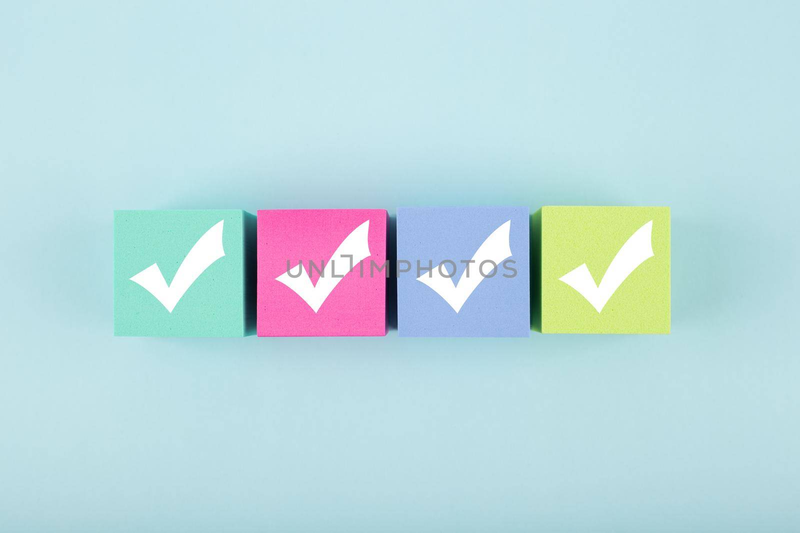 Four checkmarks on multicolored cubes in a row on blue background with copy space. Concept of questionary, checklist, to do list, planning, business or verification. Modern minimal composition 