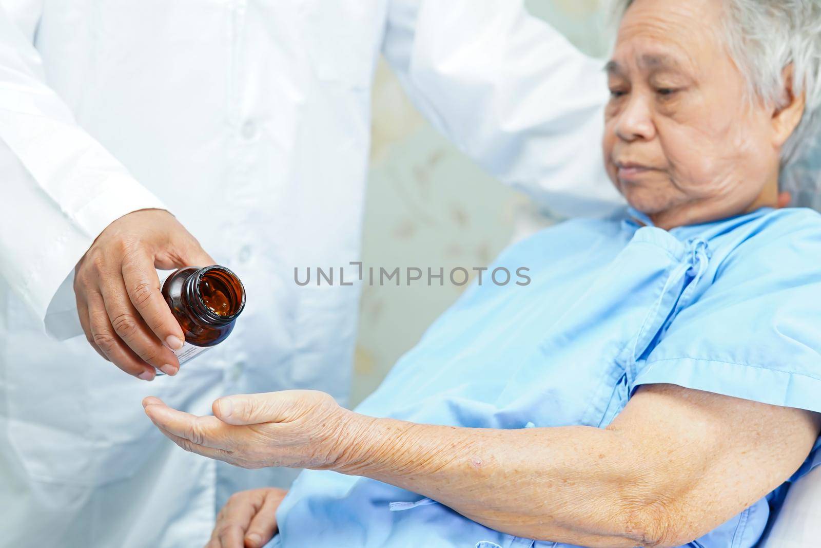 Asian doctor holding and pour antibiotics pills medicine from the bottle to patient for treatment infection in hospital : Pharmacy drugstore concept. by pamai