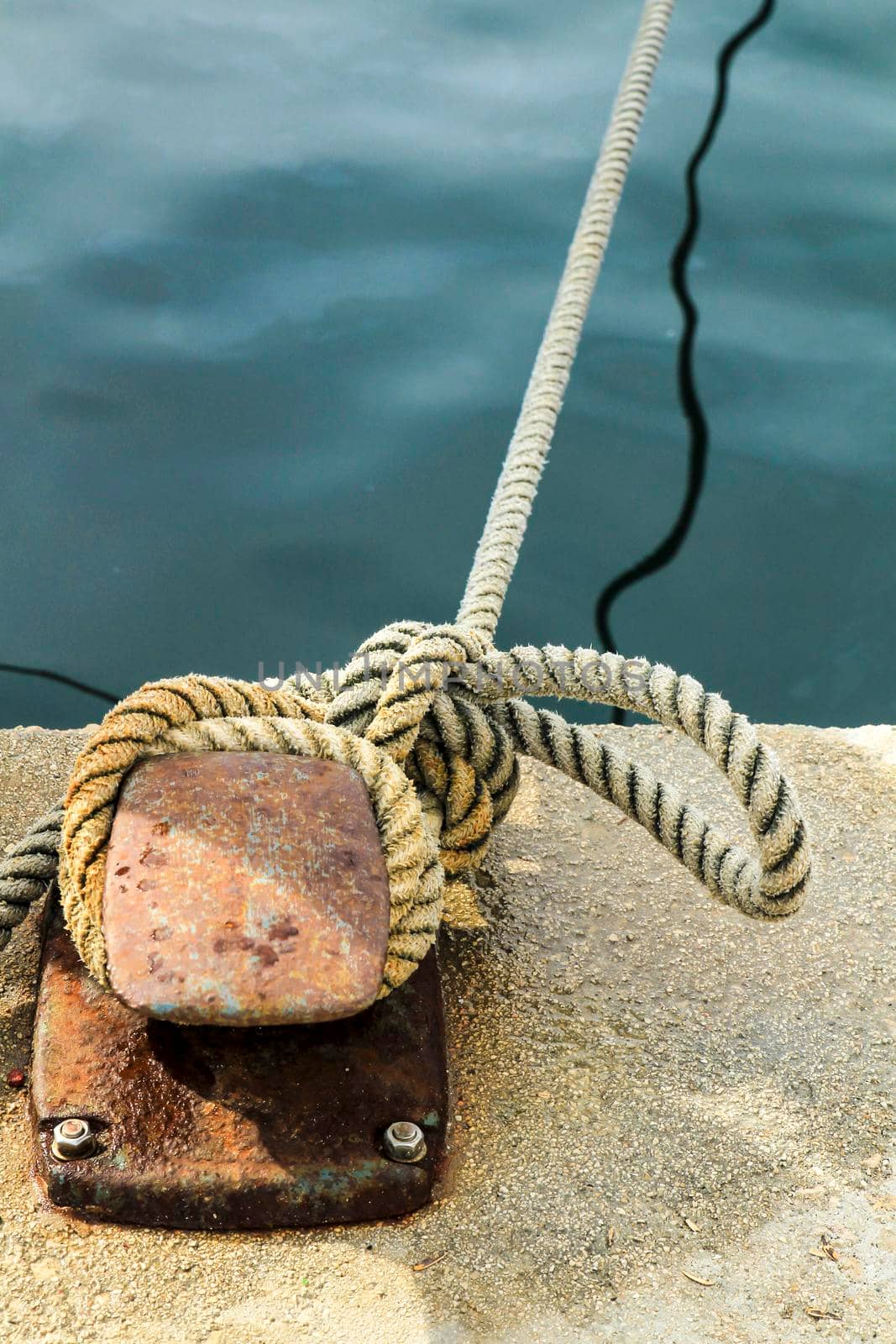 Rusty mooring bollard with tied rope in the port of Santa Pola, Alicante, Spain