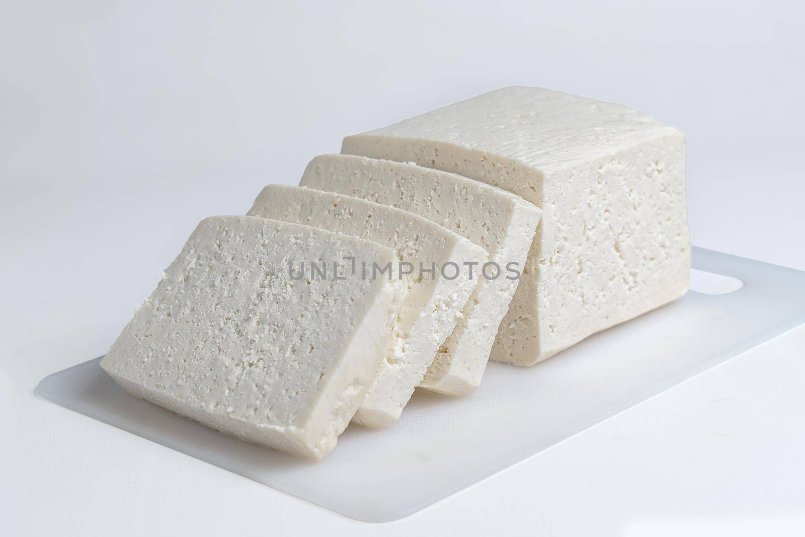 White cheese cut into several pieces on a white surface and white background