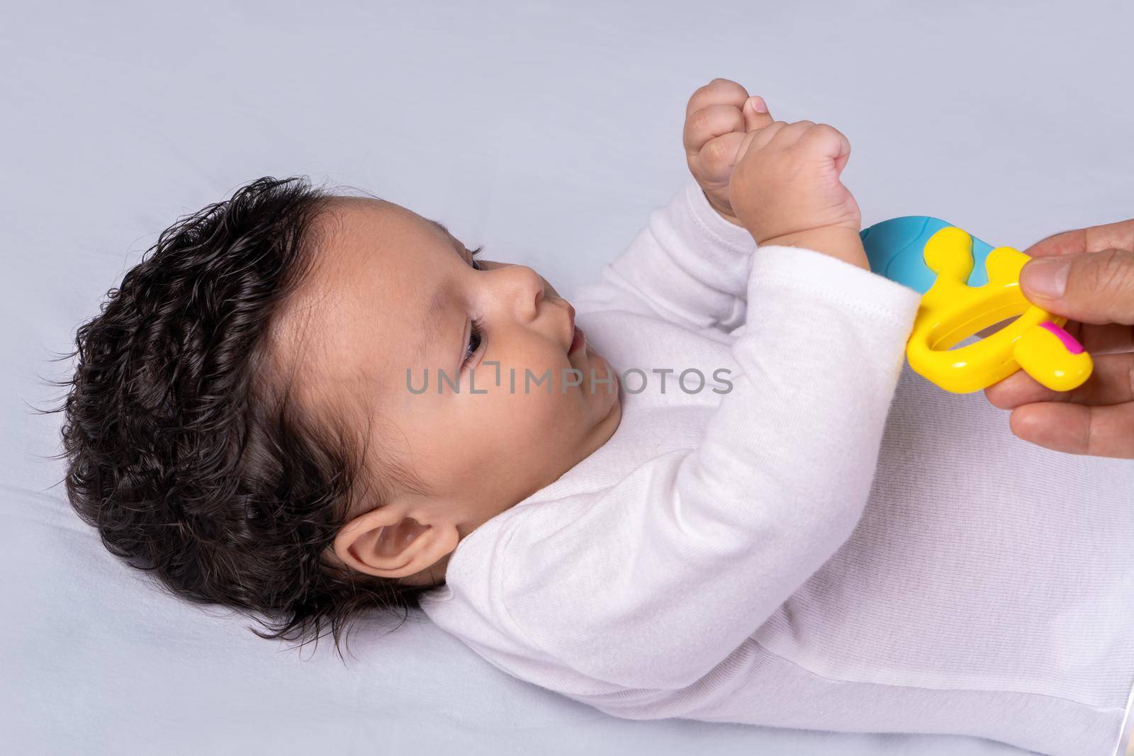 Infant lying on his back with his hands up trying to grab a toy