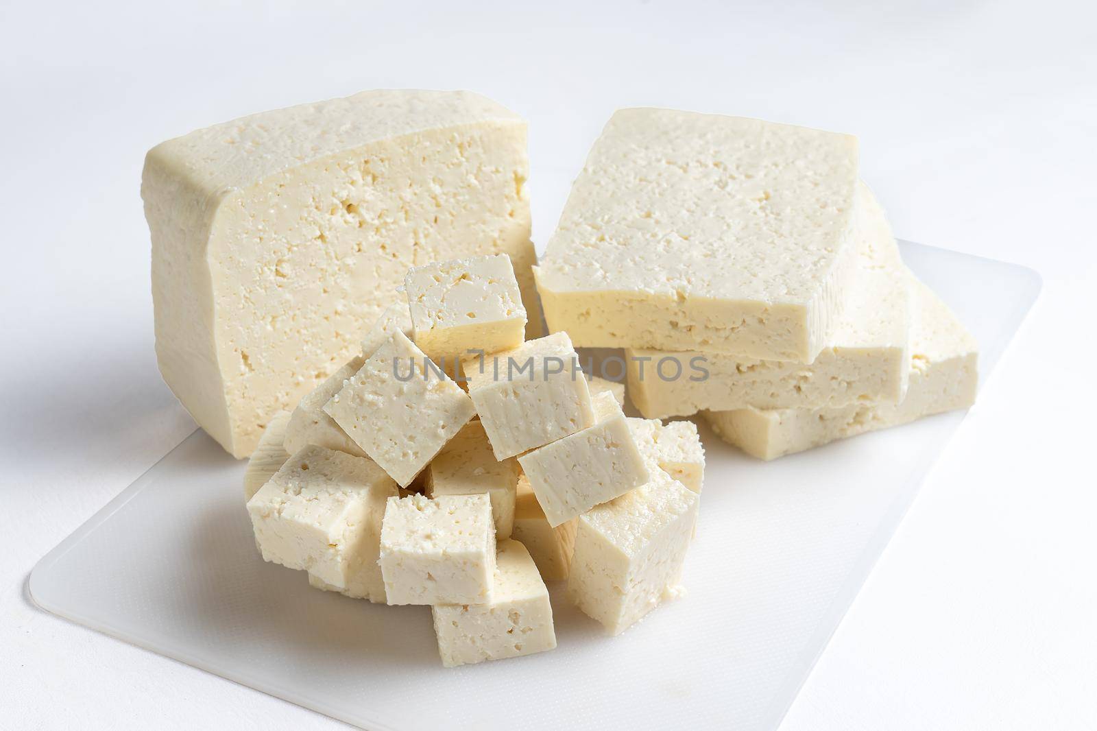 White cheese cut into several pieces on a white surface and white background