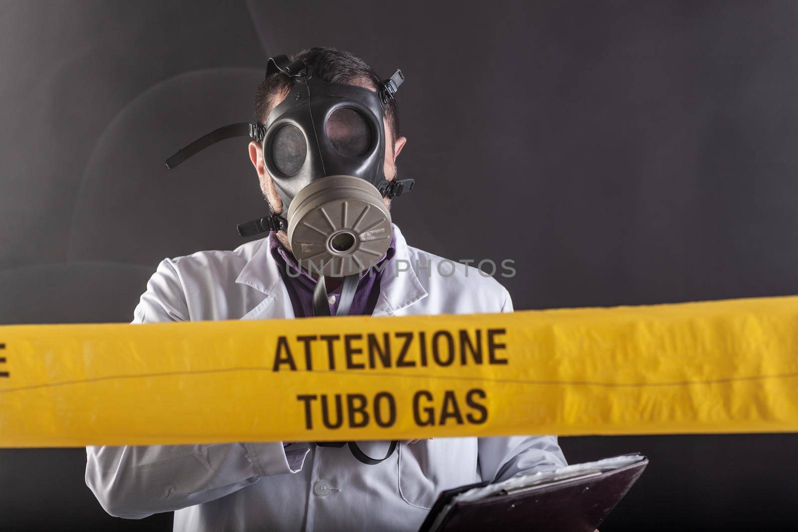 A medical engineer wearing antigas mask experienced in the gas leaks crisis directing the emergency during the chaos. On the yellow tape the written notice "attention gas tube"