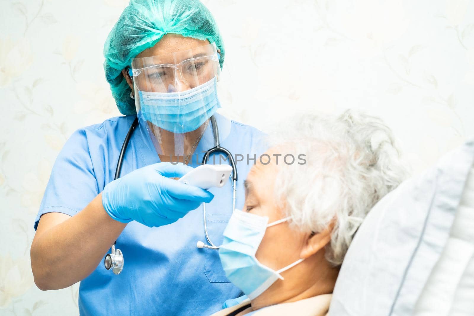 Doctor holding digital thermometer to measures asian senior or elderly old lady woman patient wearing a face mask have a fever in hospital, healthy strong medical concept. by pamai