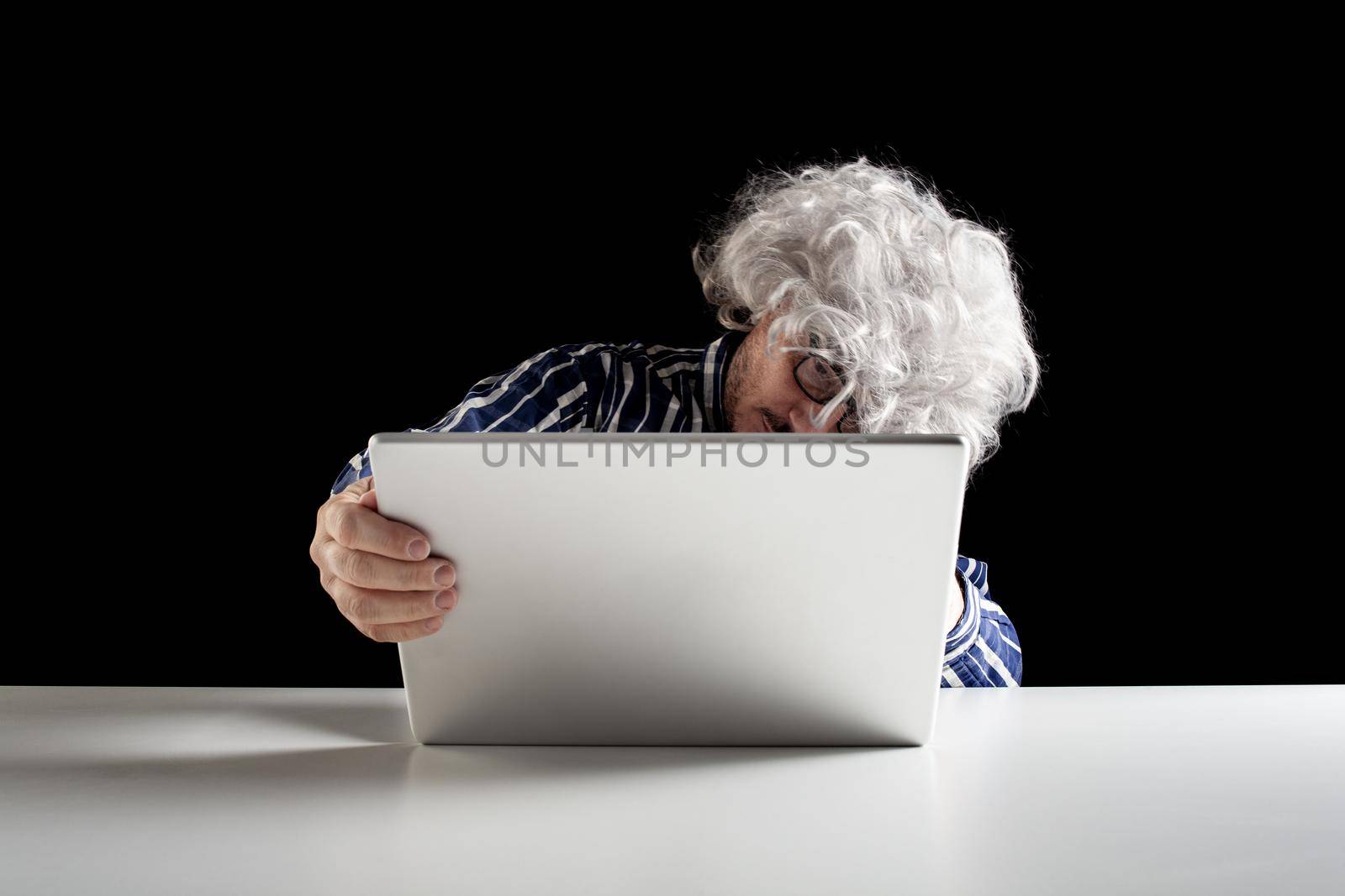 An elderly man does not know how to use the computer. He holds the laptop in his hand without knowing how to turn it on