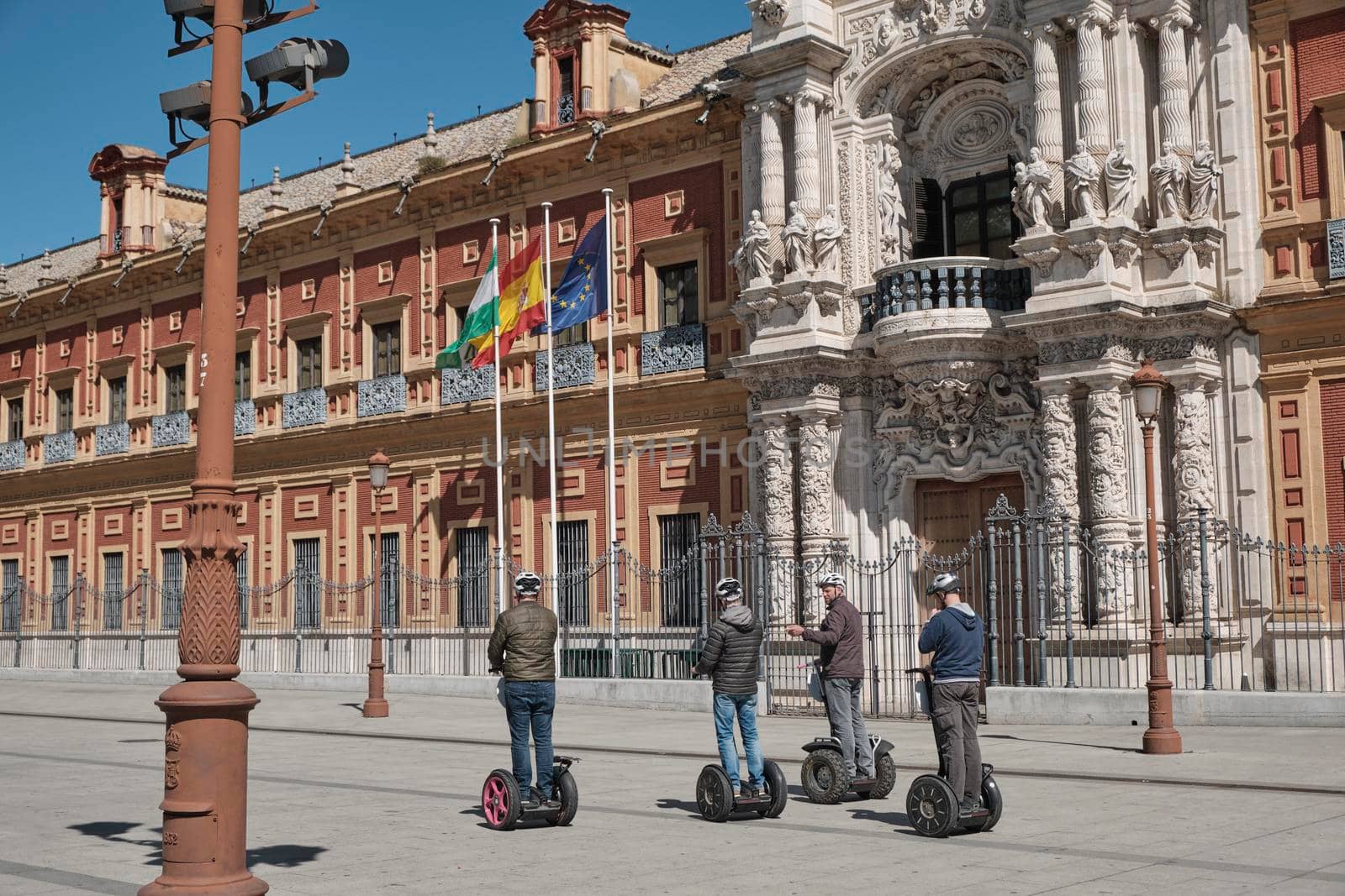 April 2019 - peoples on scooter electric skateboard intelligent hoverboard alternative way if visiting the city and view of San Telmo Palace, Seville, Spain. Seat of the presidency in a sunny day