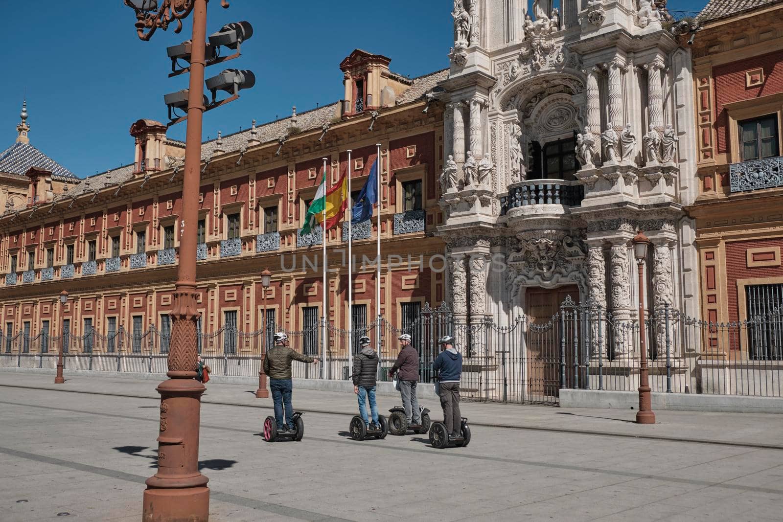 April 2019 - peoples on scooter electric skateboard intelligent hoverboard alternative way if visiting the city and view of San Telmo Palace, Seville, Spain. Seat of the presidency in a sunny day. by Sandronize