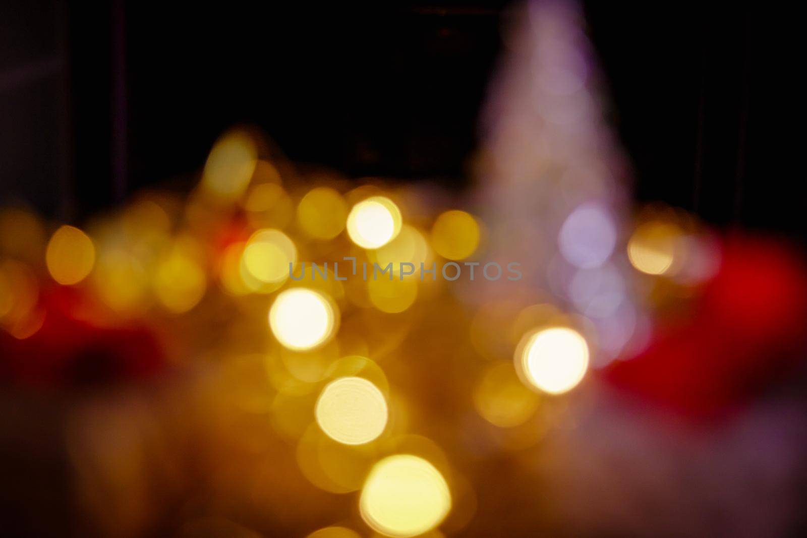 Christmas New Year boxes with a red bow. Yellow garland, light in dark room out of focus. Artistic bokeh.