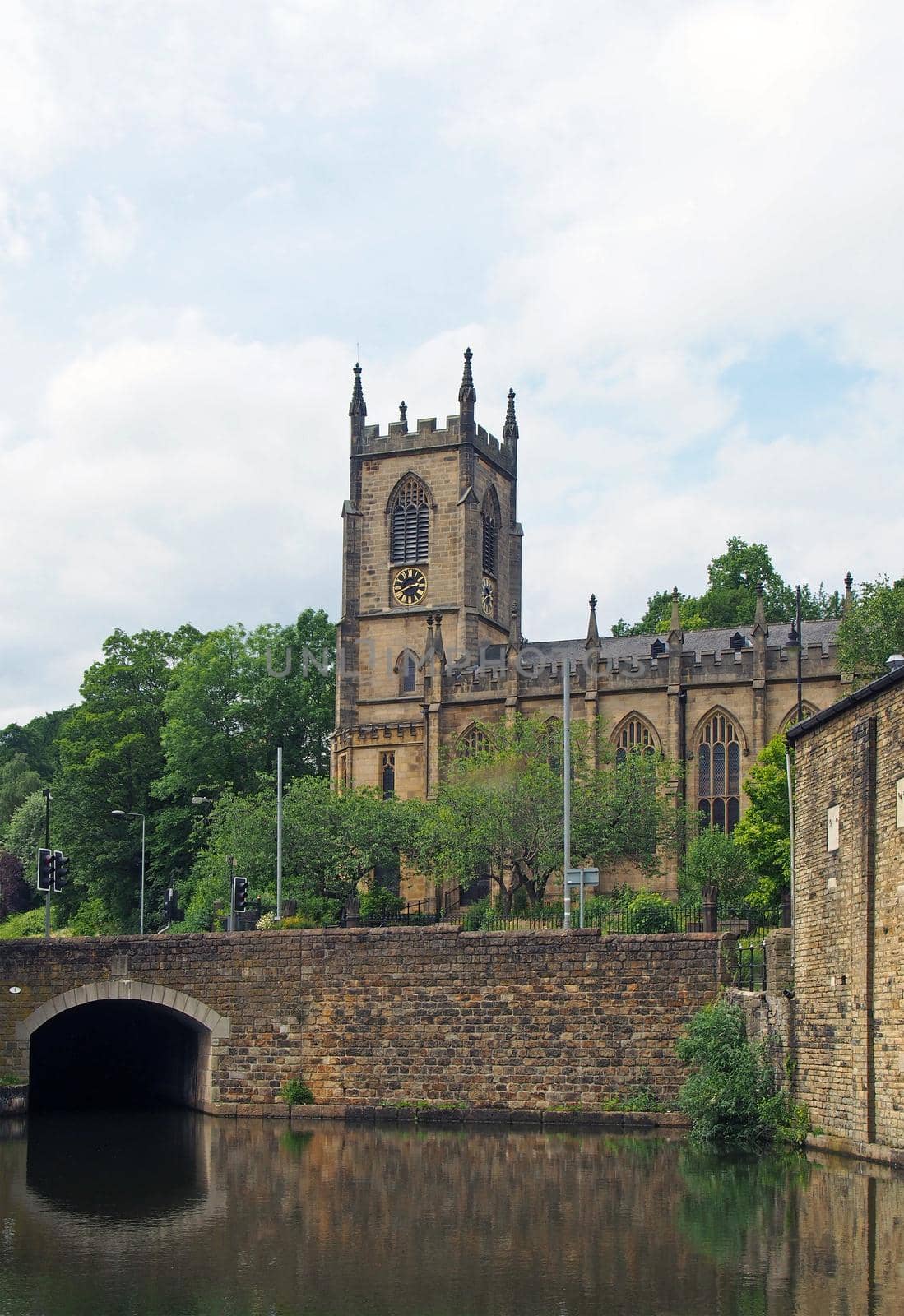 a stone bridge crossing the canal in sowerby bridge west yorkshire with the historic christ church building surrounded by trees by philopenshaw