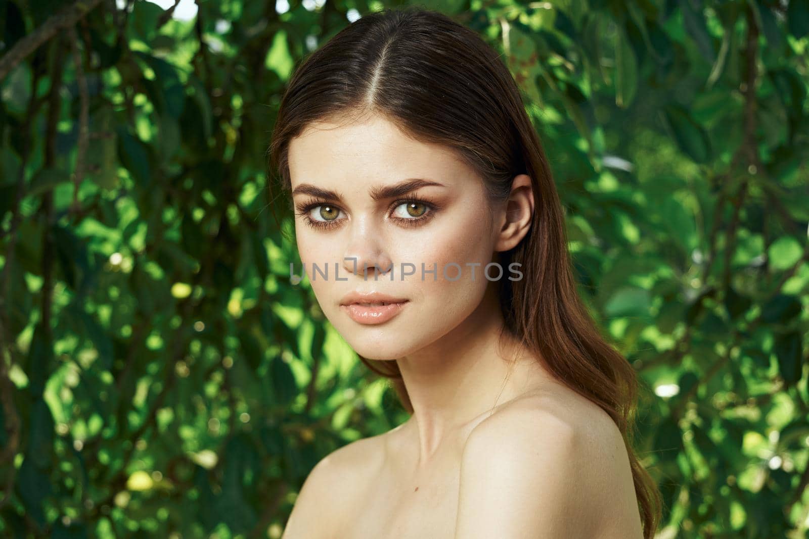 smiling woman attractive look bare shoulders green leaves close-up. High quality photo