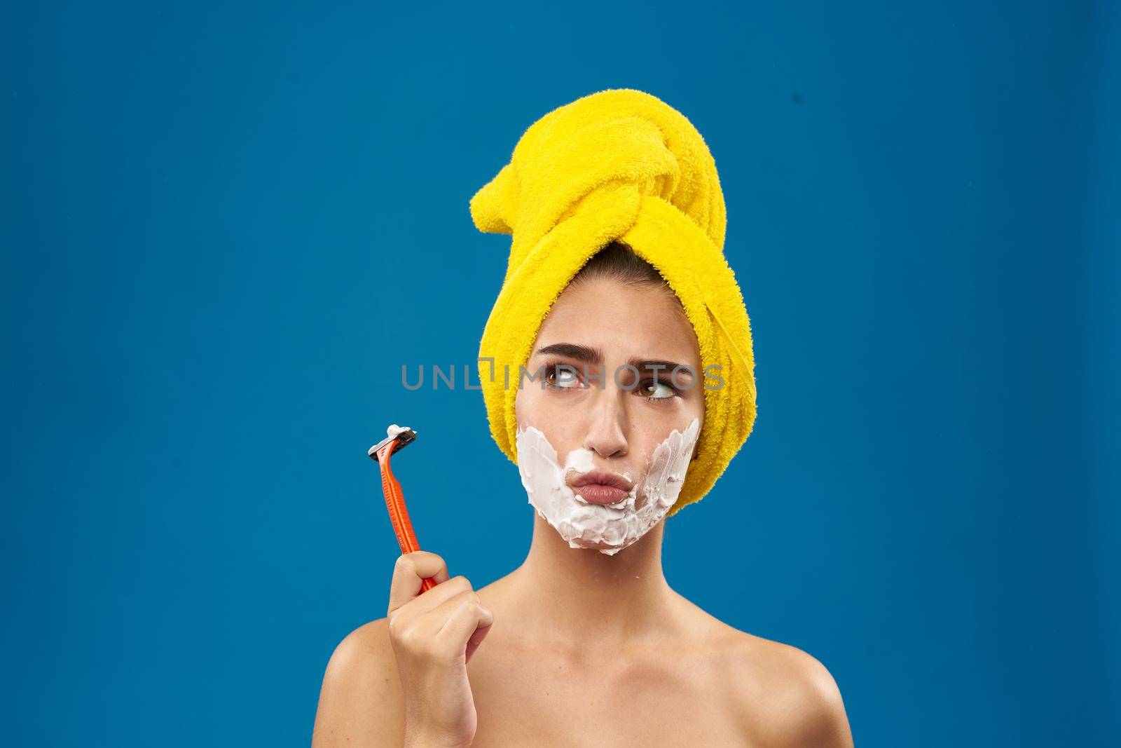 cheerful woman with a yellow towel on his head shaving blue background. High quality photo