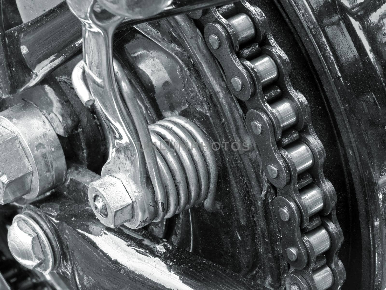 monochrome close up of the drive chain on a black vintage motorbike with chrome fixtures and steel bolts by philopenshaw