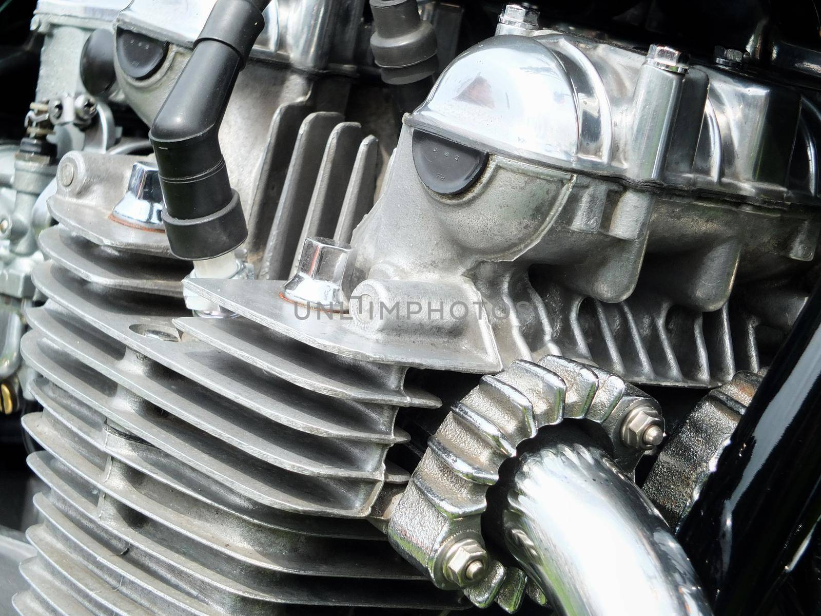 close up detail of the engine of an old vintage motorcycle with black frame and shiny chrome exhaust pipes