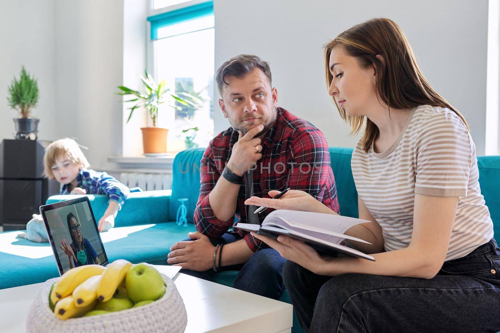 Telemedicine, technology, middle aged couple using laptop for video meeting with doctor. Husband and wife at home on the couch with child listening and talking to the doctor.