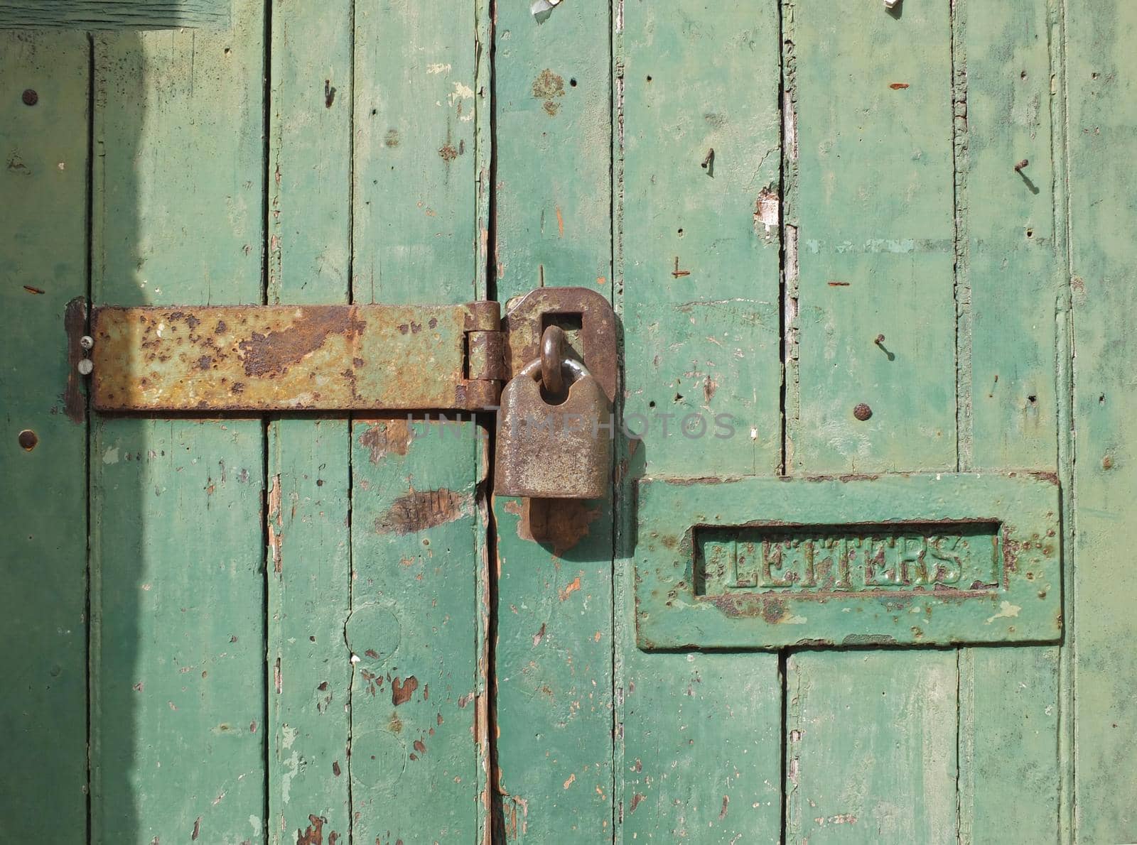 close up of an old wooden door with green faded paint and a rusty closed padlock and old metal letterbox by philopenshaw