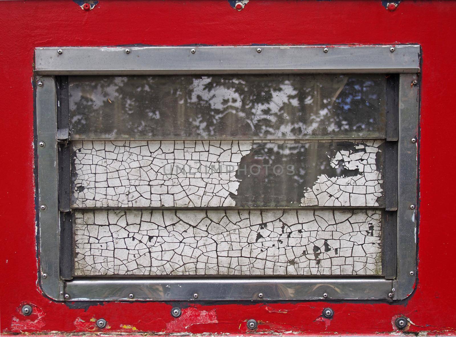 an old scruffy caravan window with steel frame and slatted windows with cracked old white paint with a red surround with rivets by philopenshaw