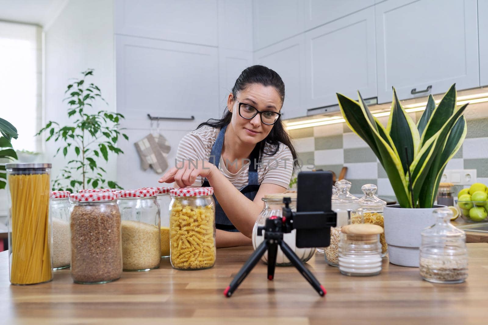 Housewife recording video reviewing products on smartphone at home in the kitchen by VH-studio