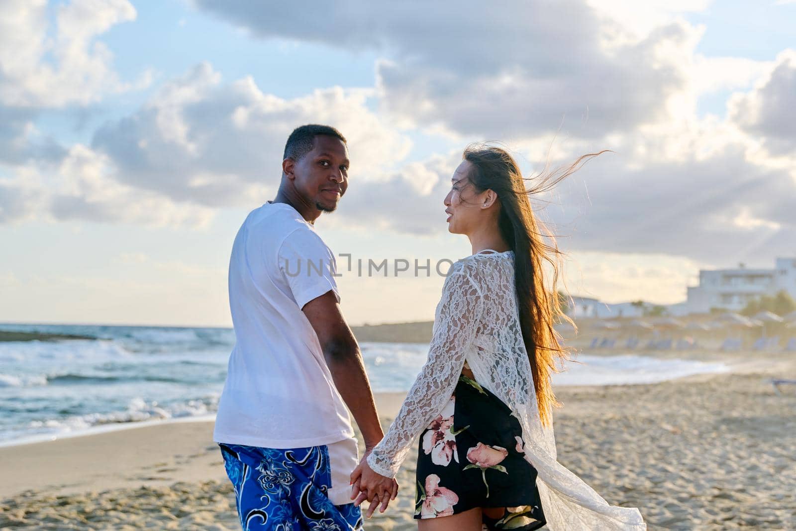 Portrait of beautiful young multiracial couple holding hands on beach. Happy loving african man and asian woman walking together. People love relationship multiethnic family, vacation, tourism concept