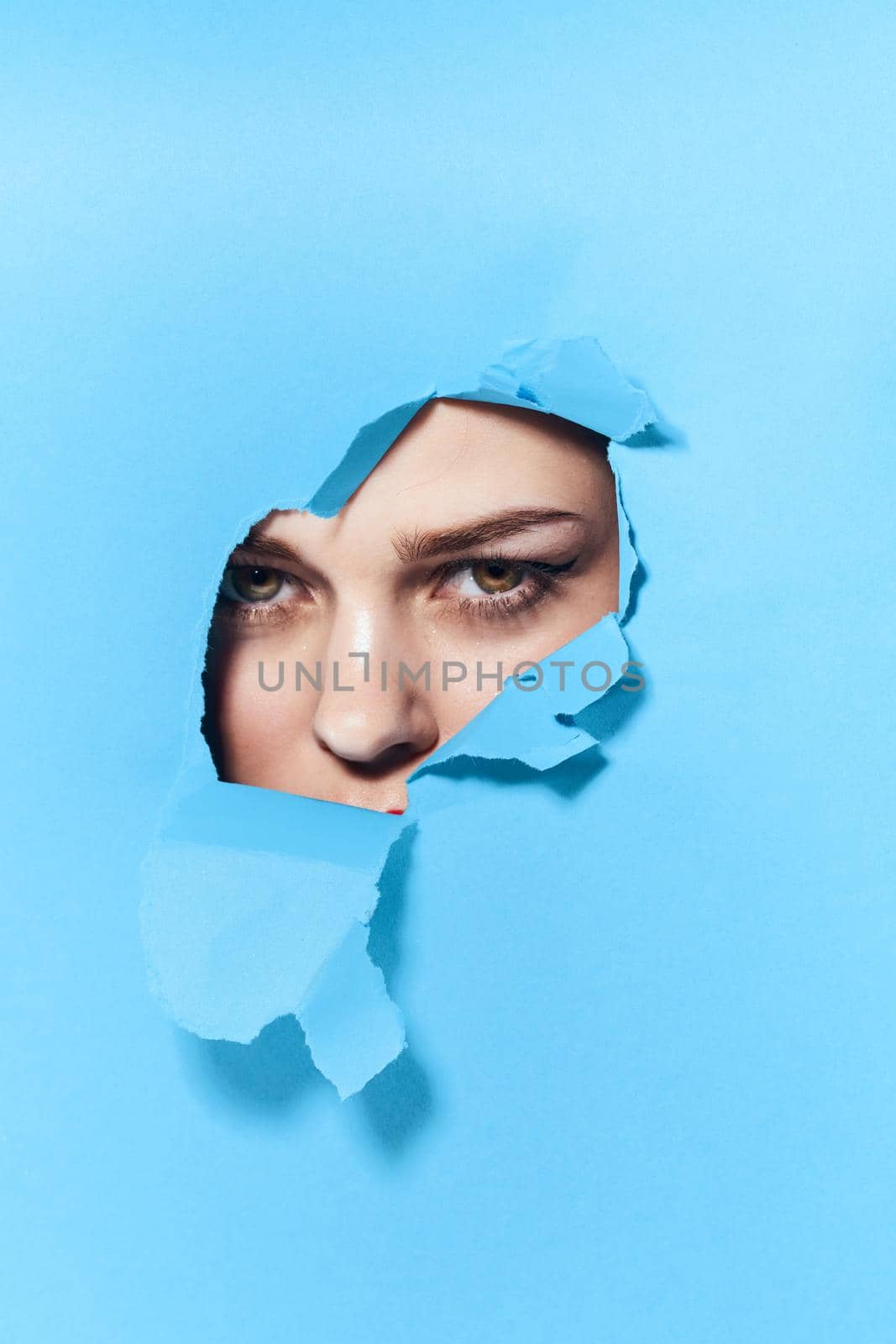 woman peeping through the holes in the poster blue studio background. High quality photo