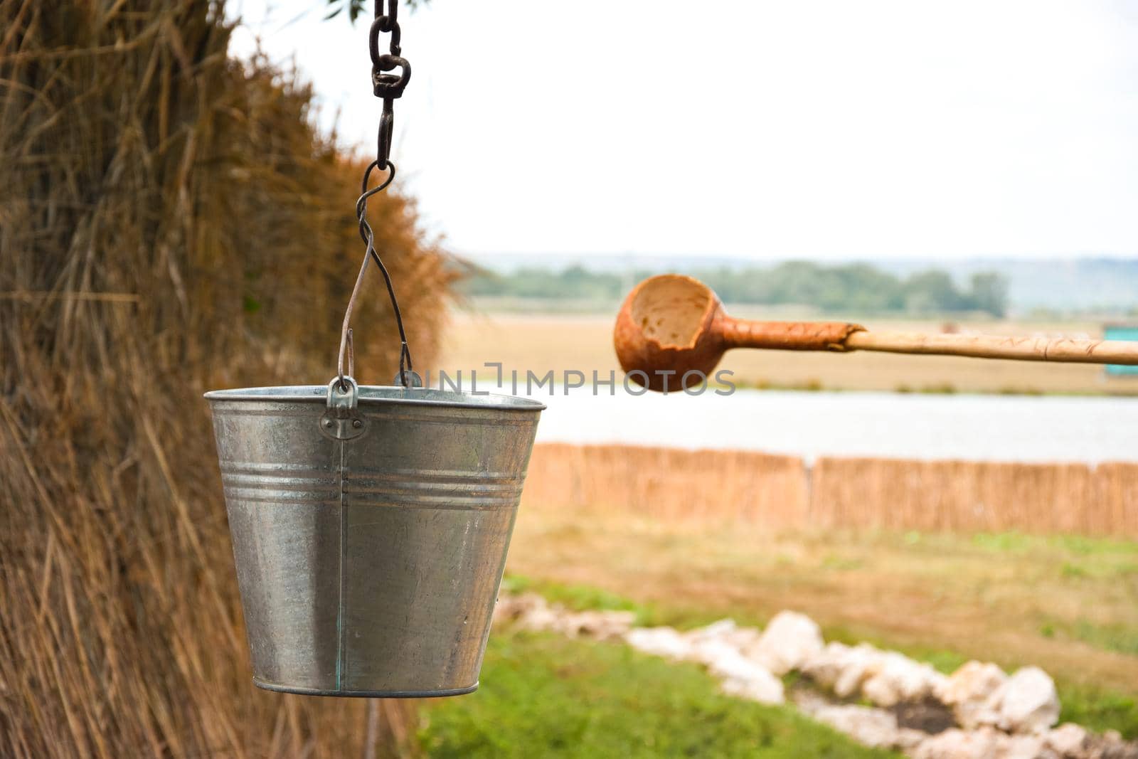 A water fountain with an old bucket and a makeshift mug made of pumpkin. Reed fence in background. Traditions and lifestyle.