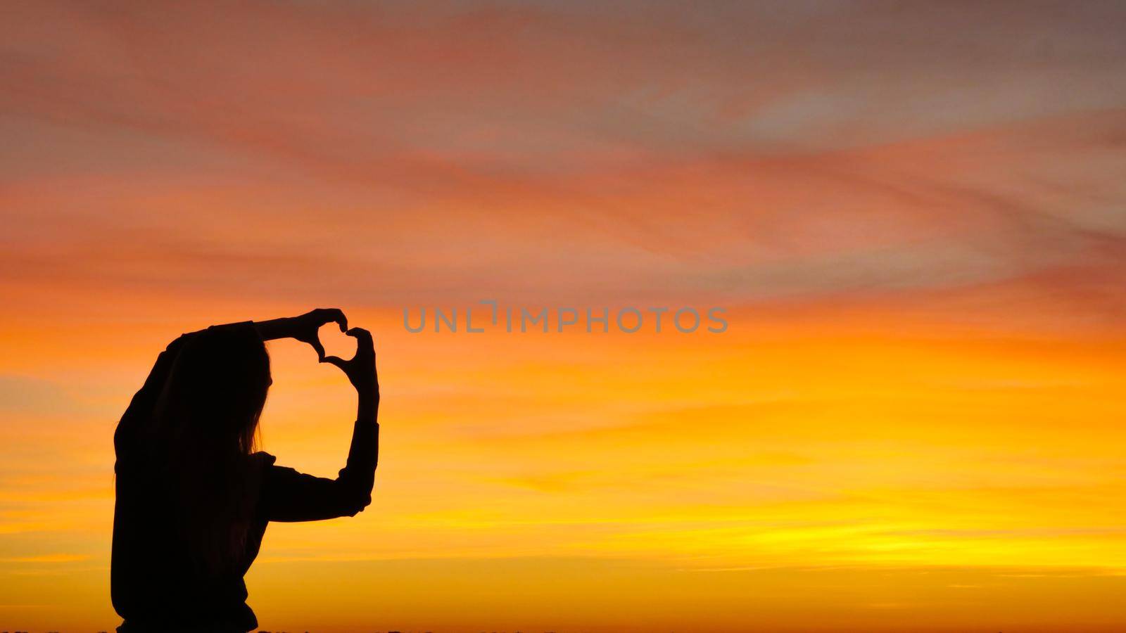 Silhouette woman forming a heart symbol at sunset